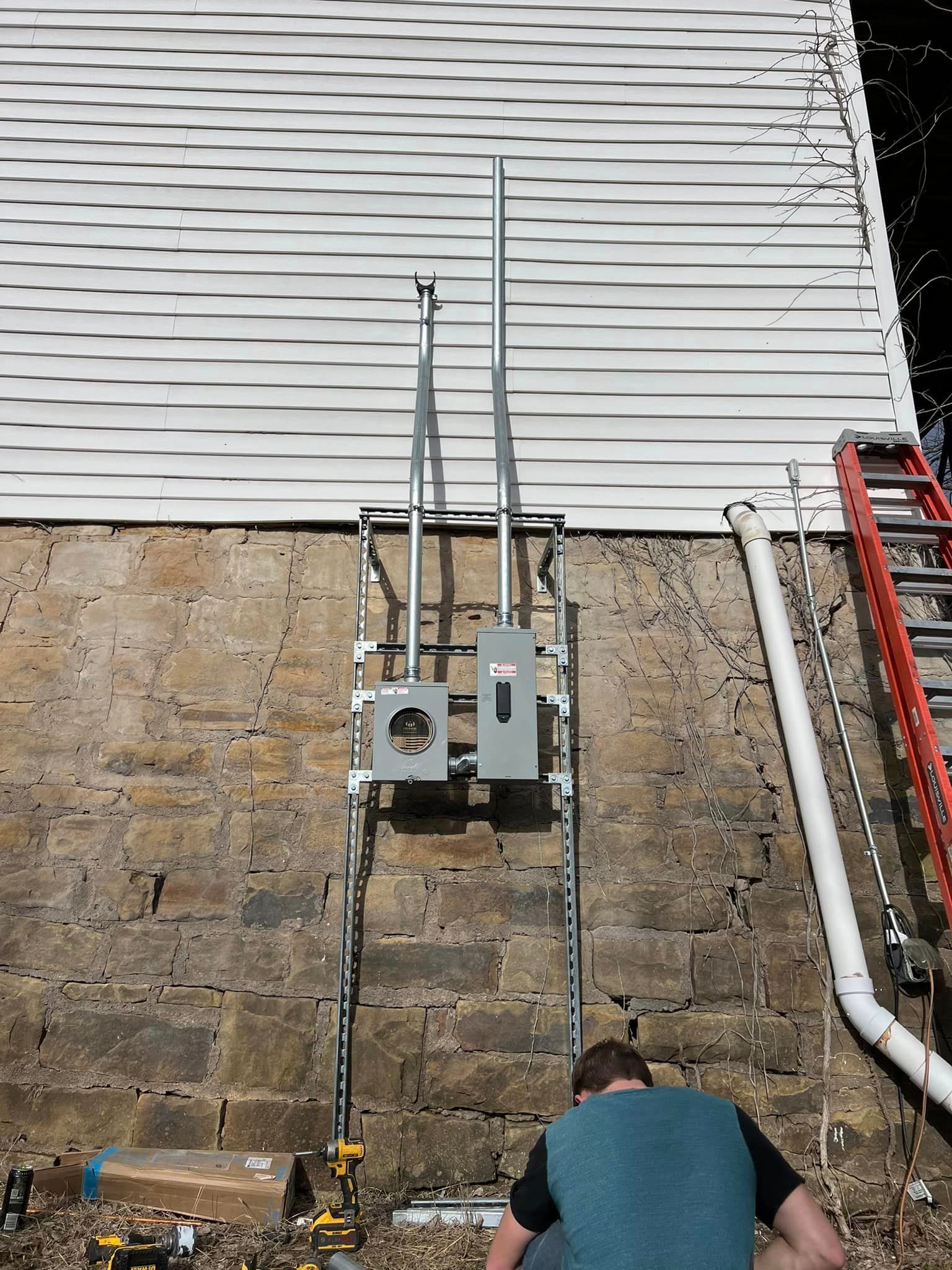A man is working on a electrical box on the side of a building