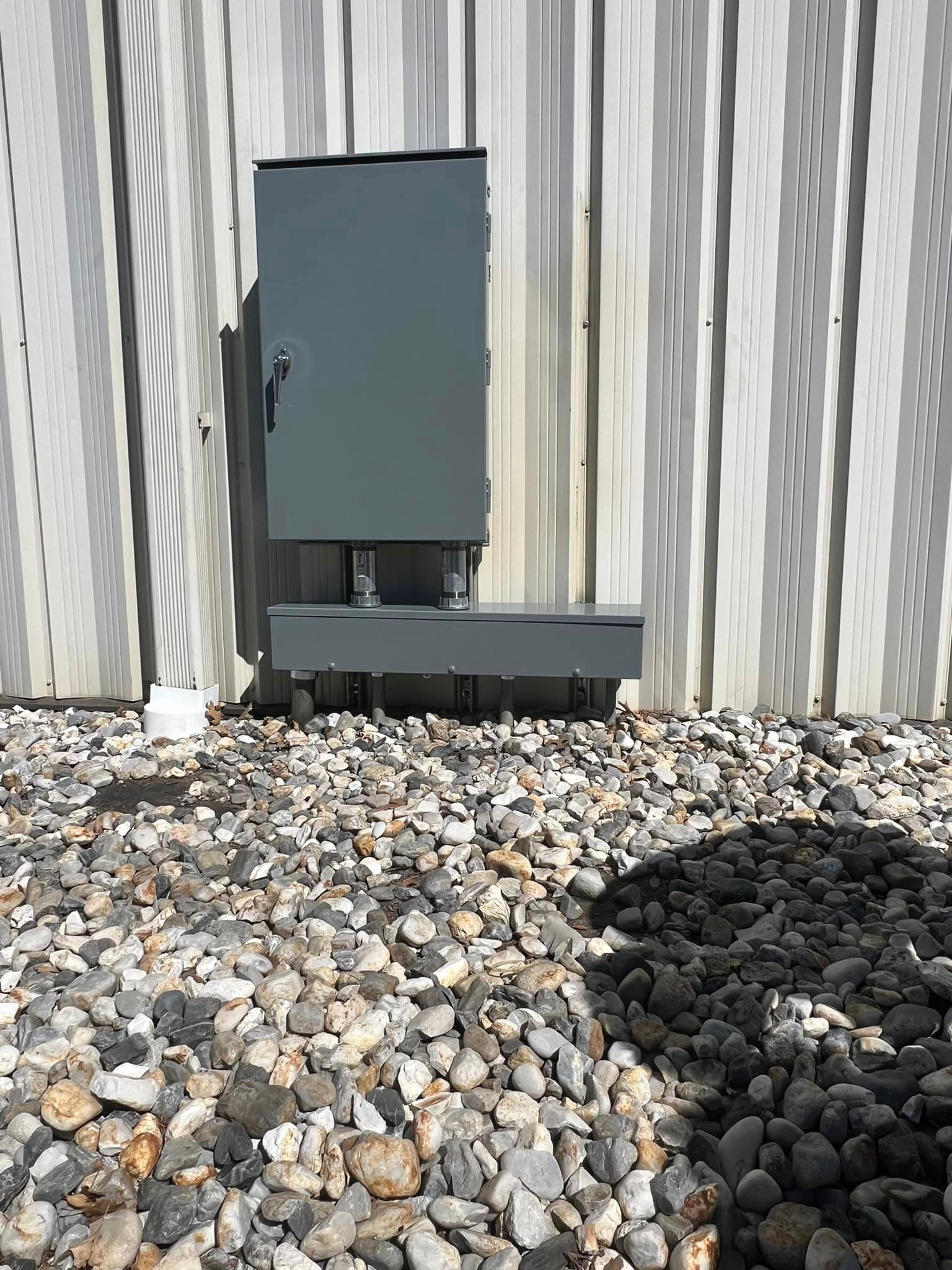 A gray box is sitting on top of a pile of rocks in front of a building.