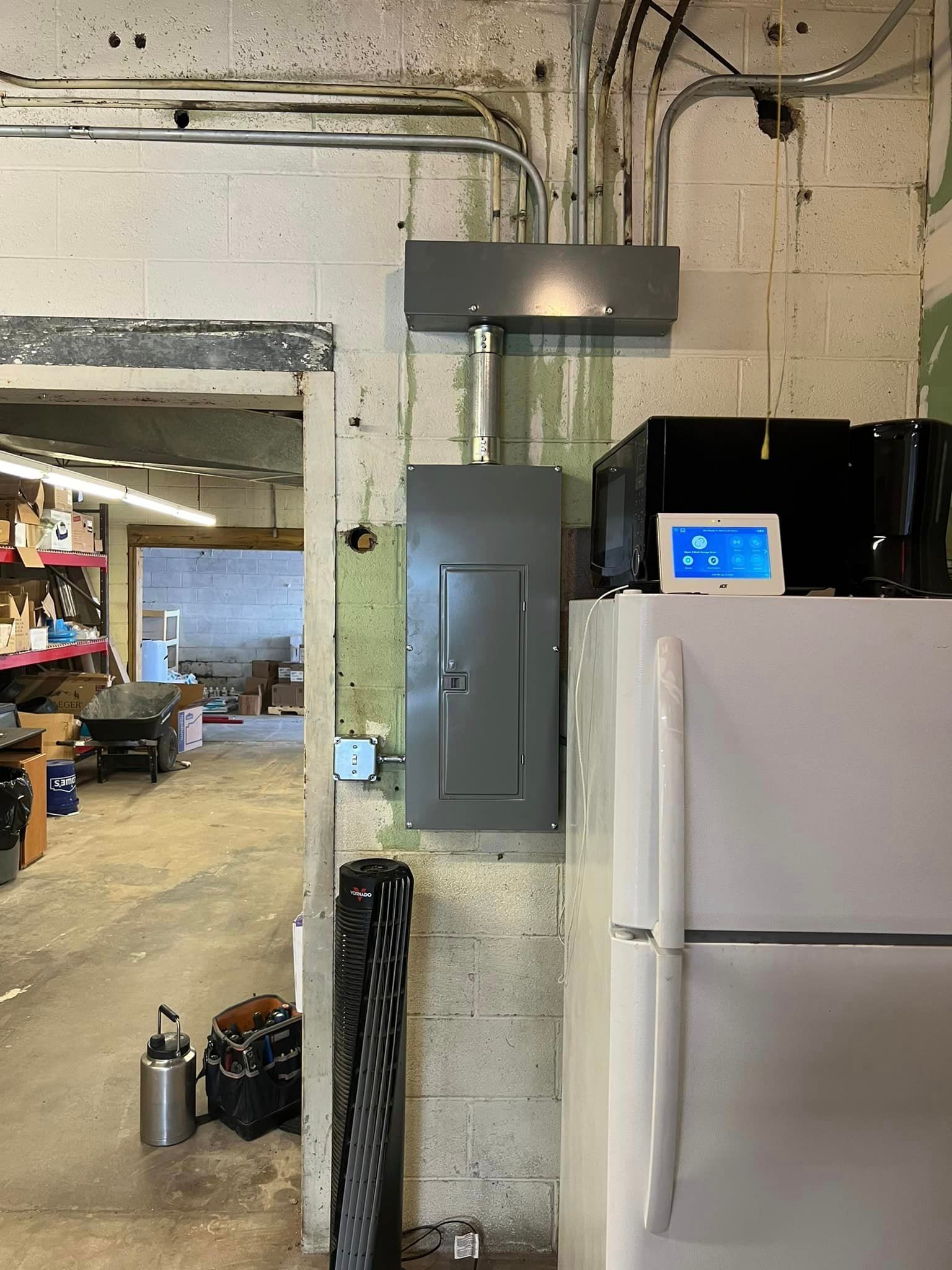 A refrigerator is sitting next to a electrical box in a garage.