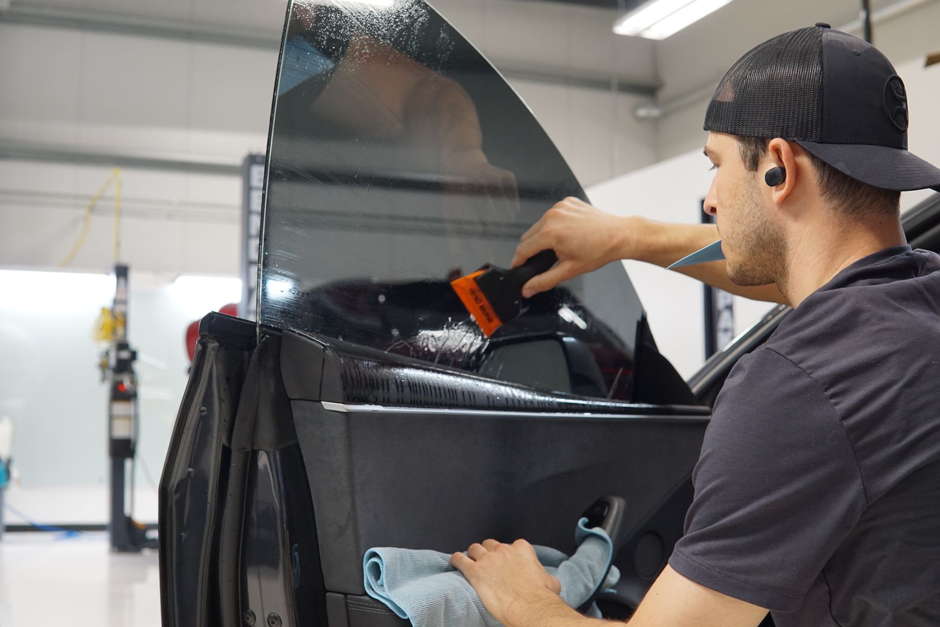 Worker installing tinted film on a car window in a workshop
