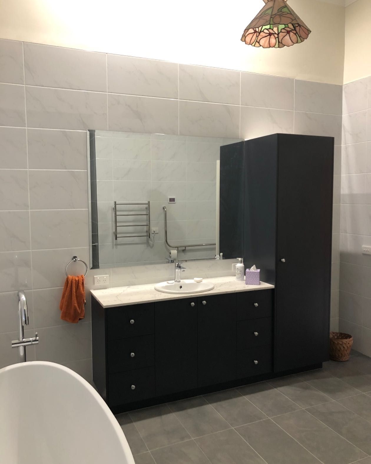 Bathroom With Dark Cabinets, Large Mirror, and Tiled Walls. a Towel Hangs Near the Sink