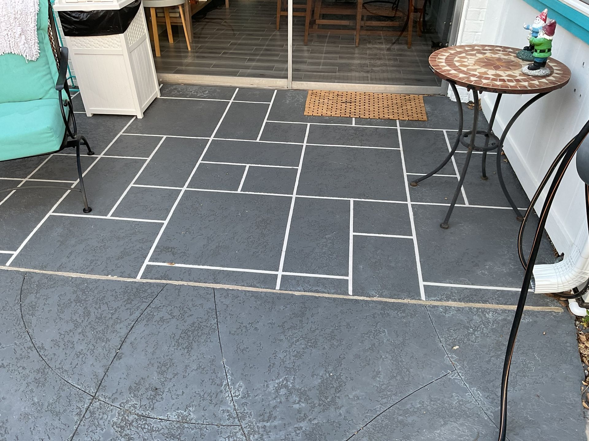 Outdoor patio with gray painted concrete and white lines, a small table, and a welcome mat.