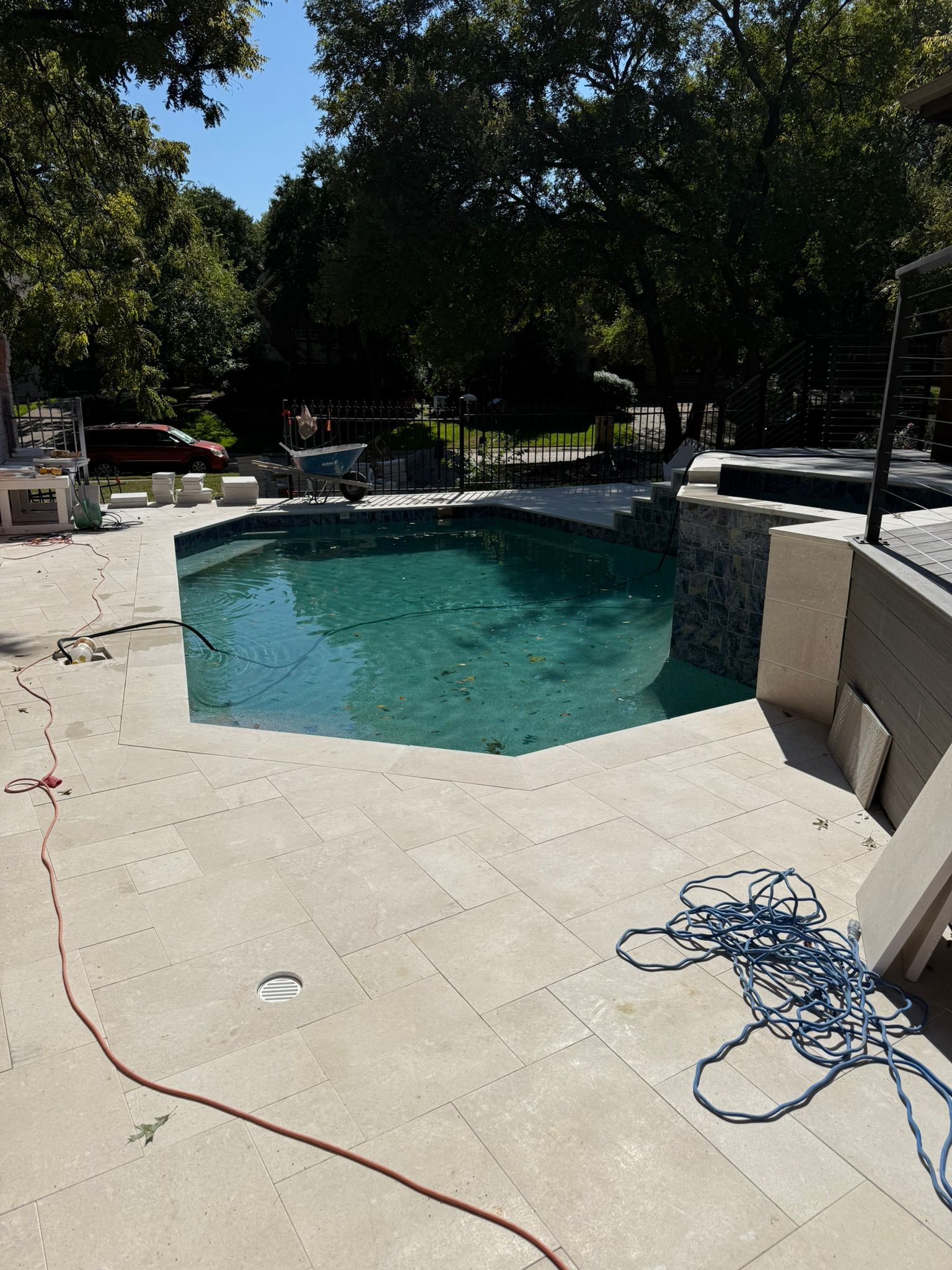 A partially completed pool with tan tiling and a blue rope, surrounded by trees on a sunny day.
