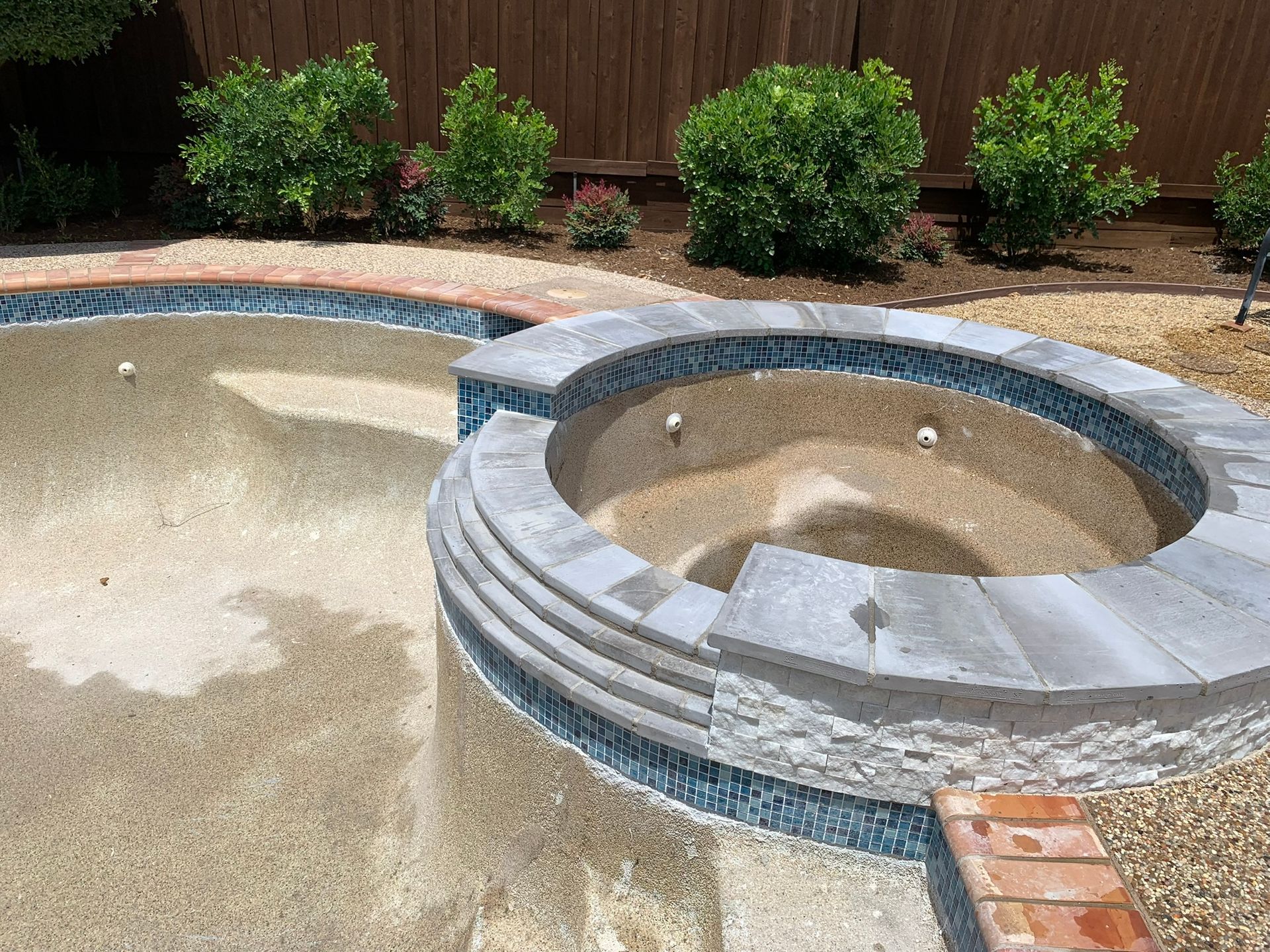 Pool with tiled edge and built-in spa. Plants in the background, surrounded by gravel and brick.