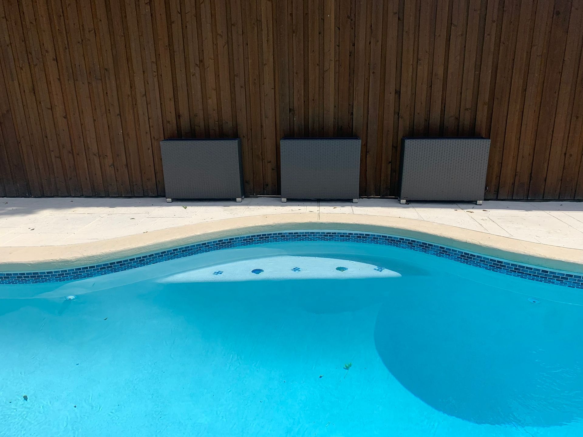 Three gray squares on a pool deck against a wood fence, with a blue pool in the foreground.