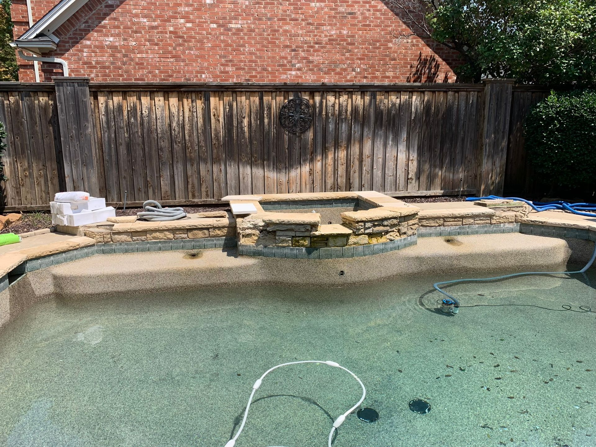 Pool with stone coping, steps, and spa against a weathered wooden fence.