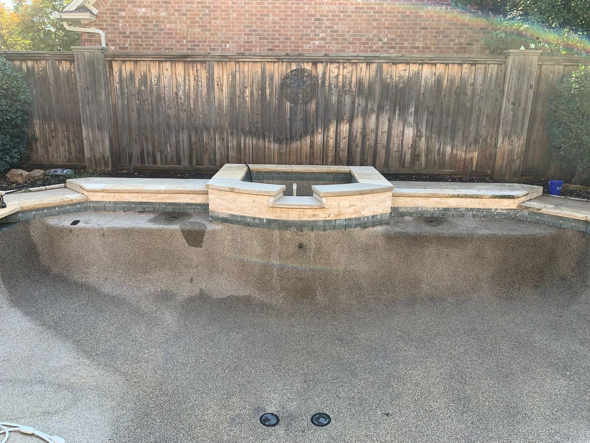 Empty swimming pool with cement borders and a wooden fence backdrop.