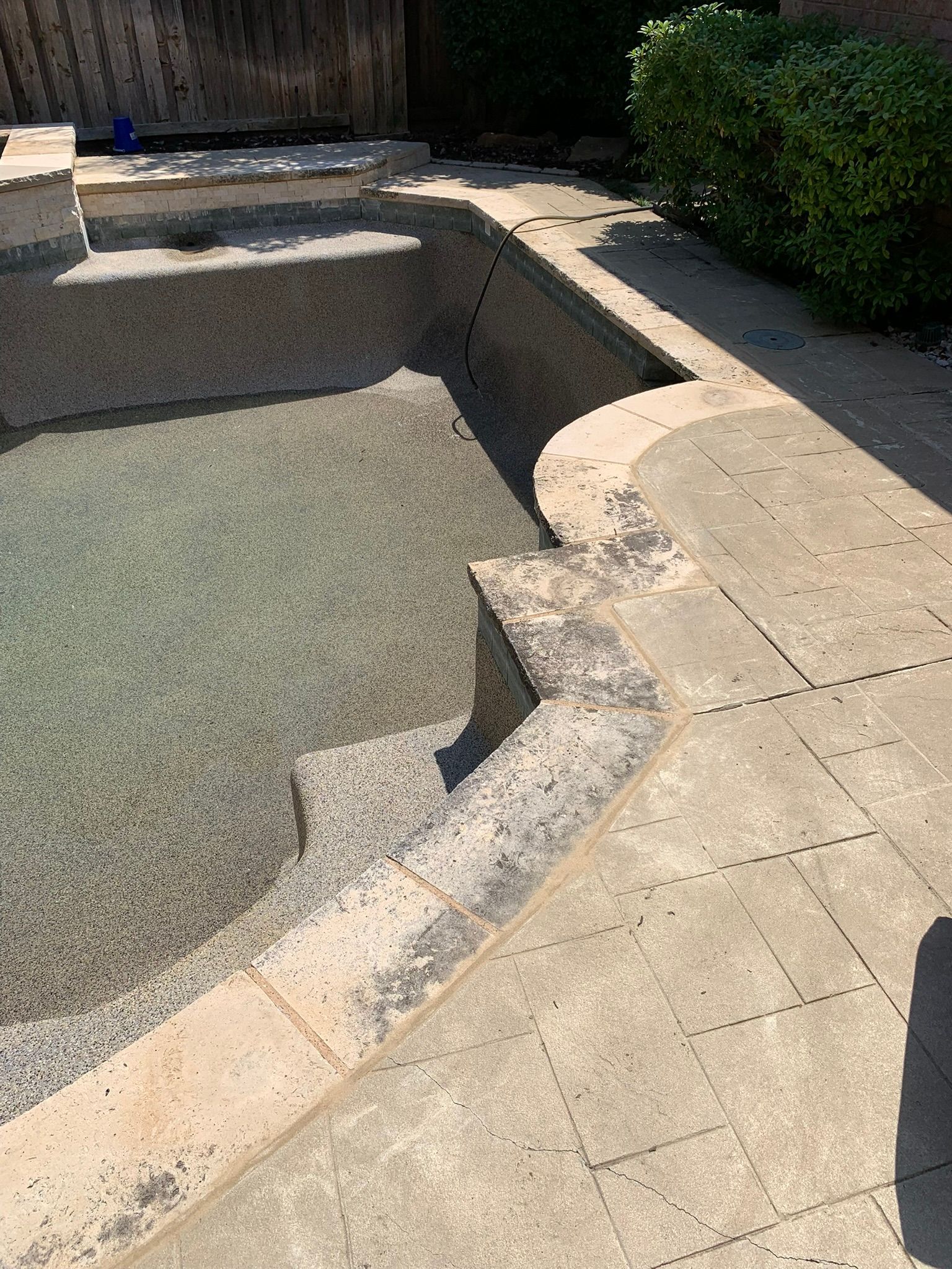 Partially filled pool with gray pebbled interior, concrete steps, and surrounding patio.