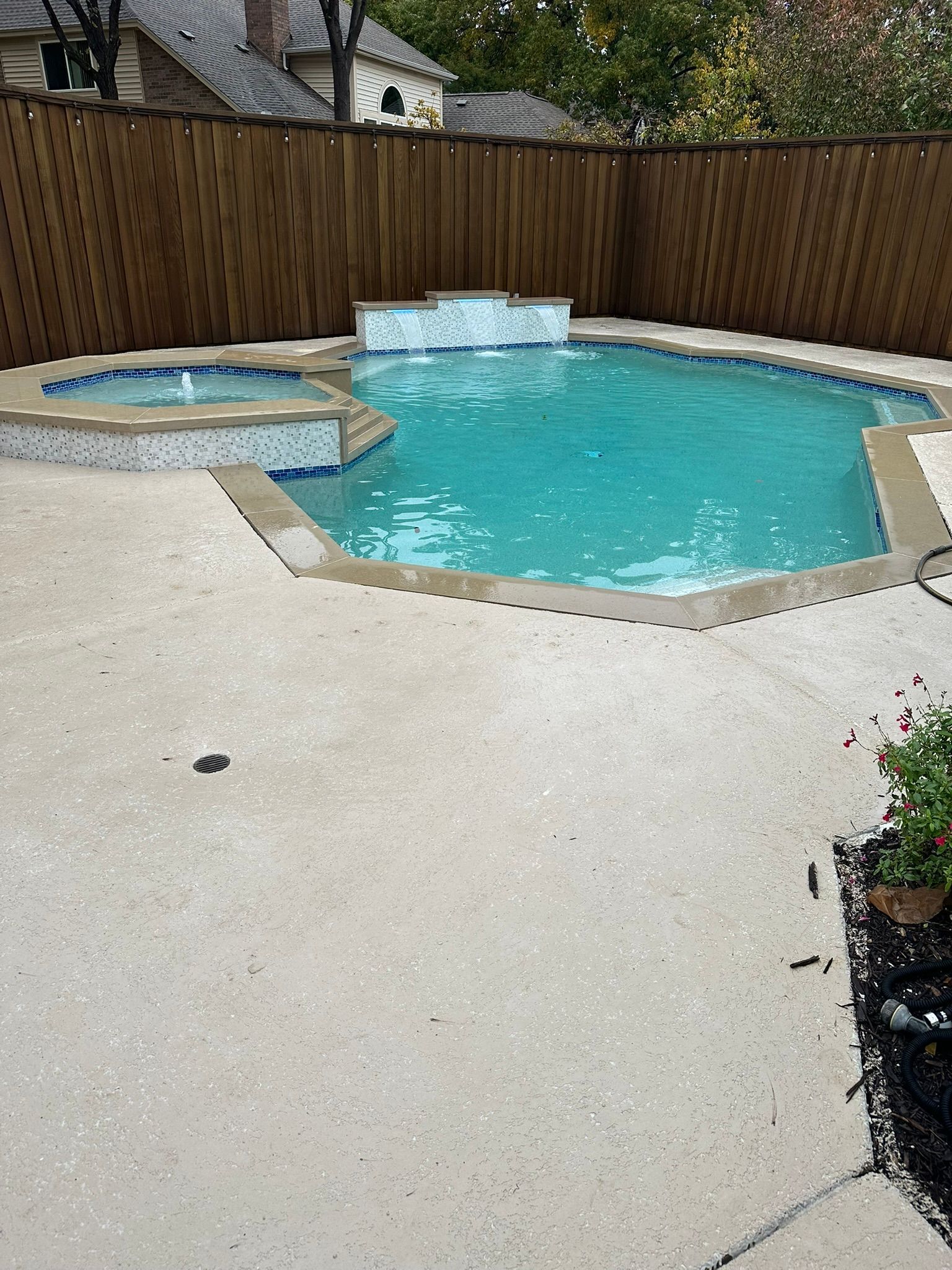 Swimming pool with turquoise water and a small hot tub. Surrounded by a concrete patio and a wooden fence.