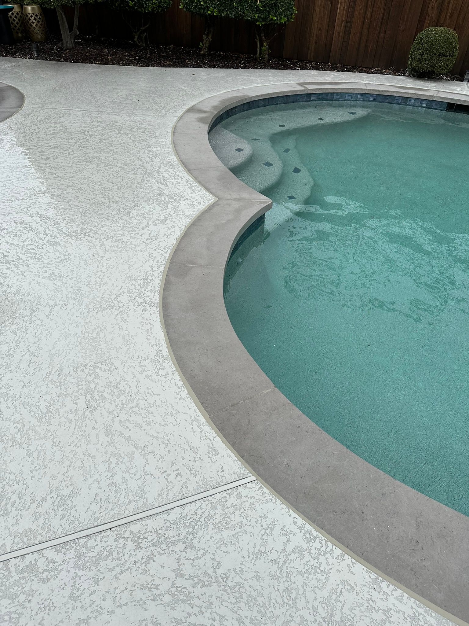 Poolside with textured concrete and steps into turquoise water.