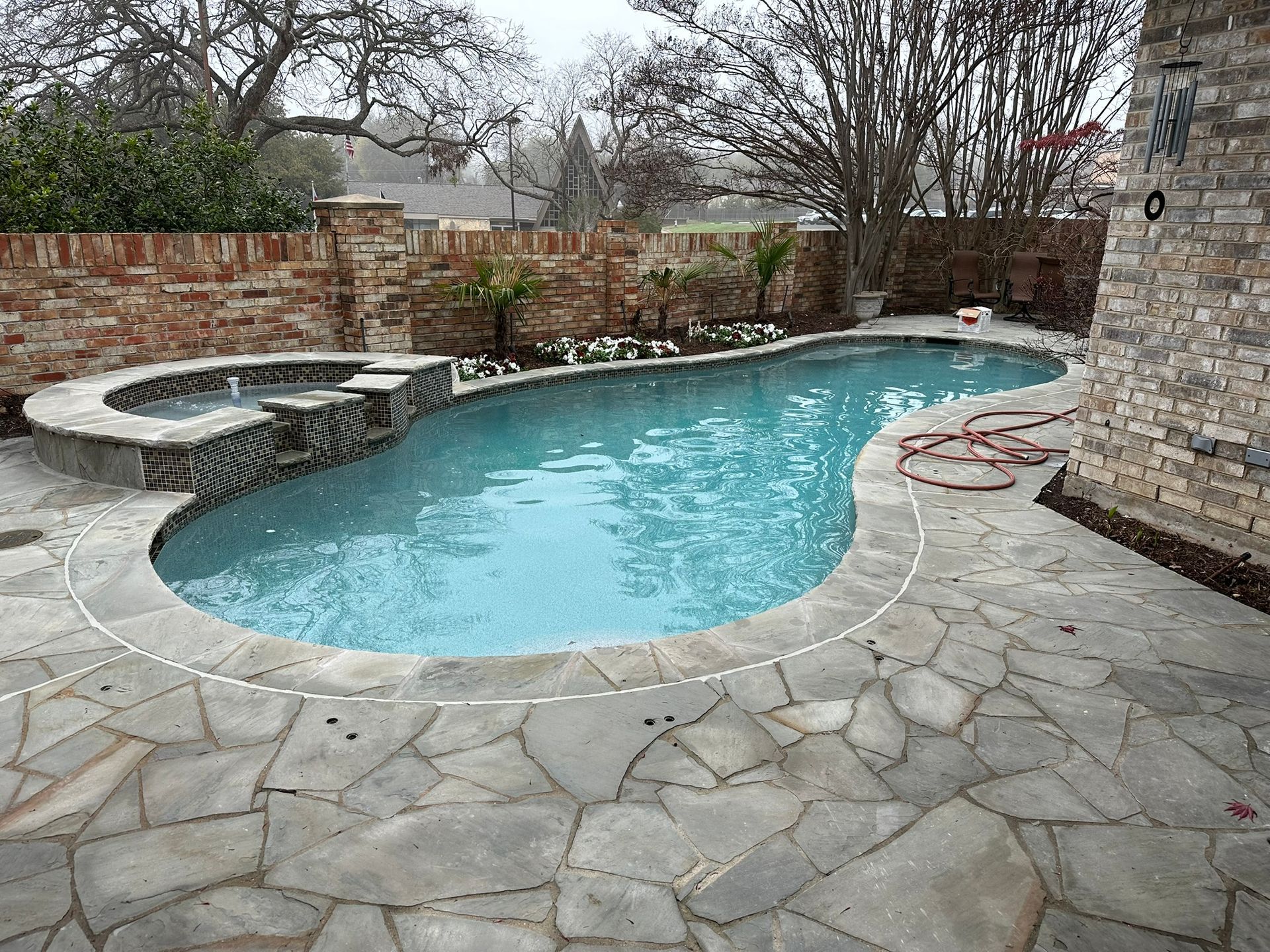 A swimming pool with a connected hot tub. Flagstone patio and brick wall surround.