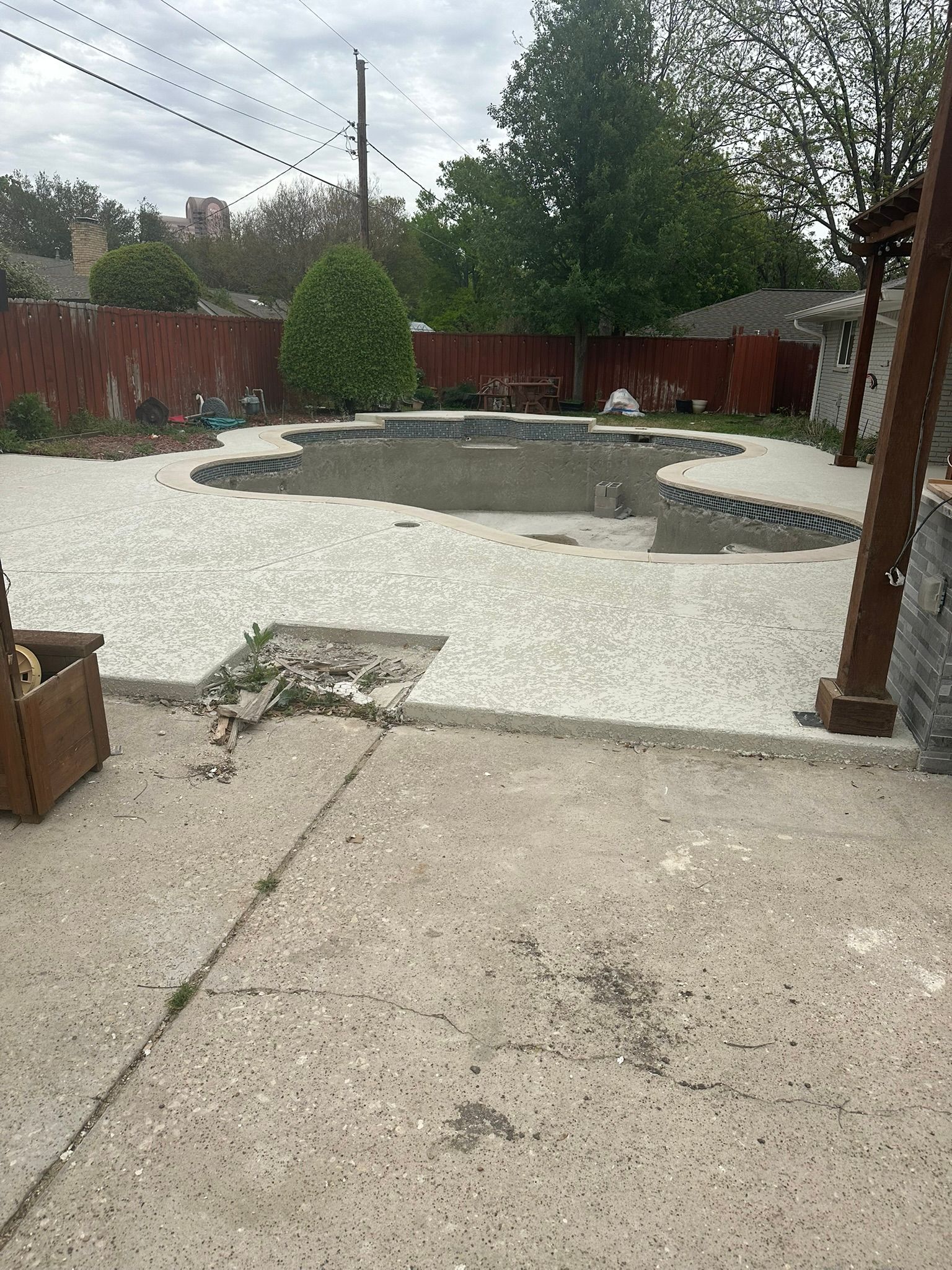 Backyard with empty pool, concrete patio, wooden fence, and power lines.