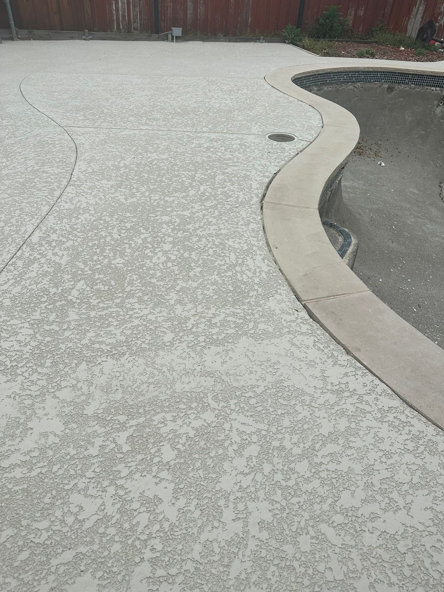 Gray speckled concrete patio with a curved border surrounding a dry pool.