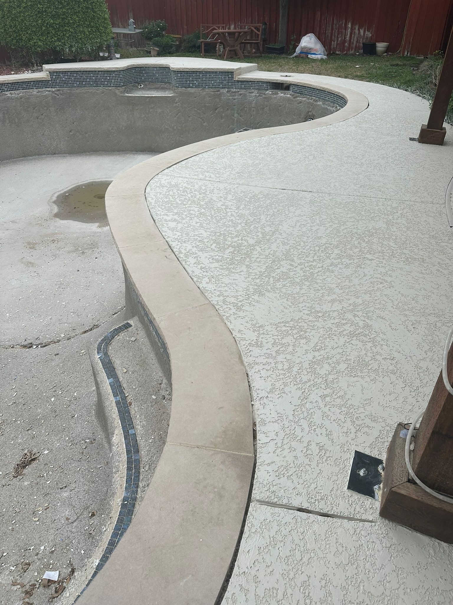 Concrete pool deck with curved edge and empty pool.