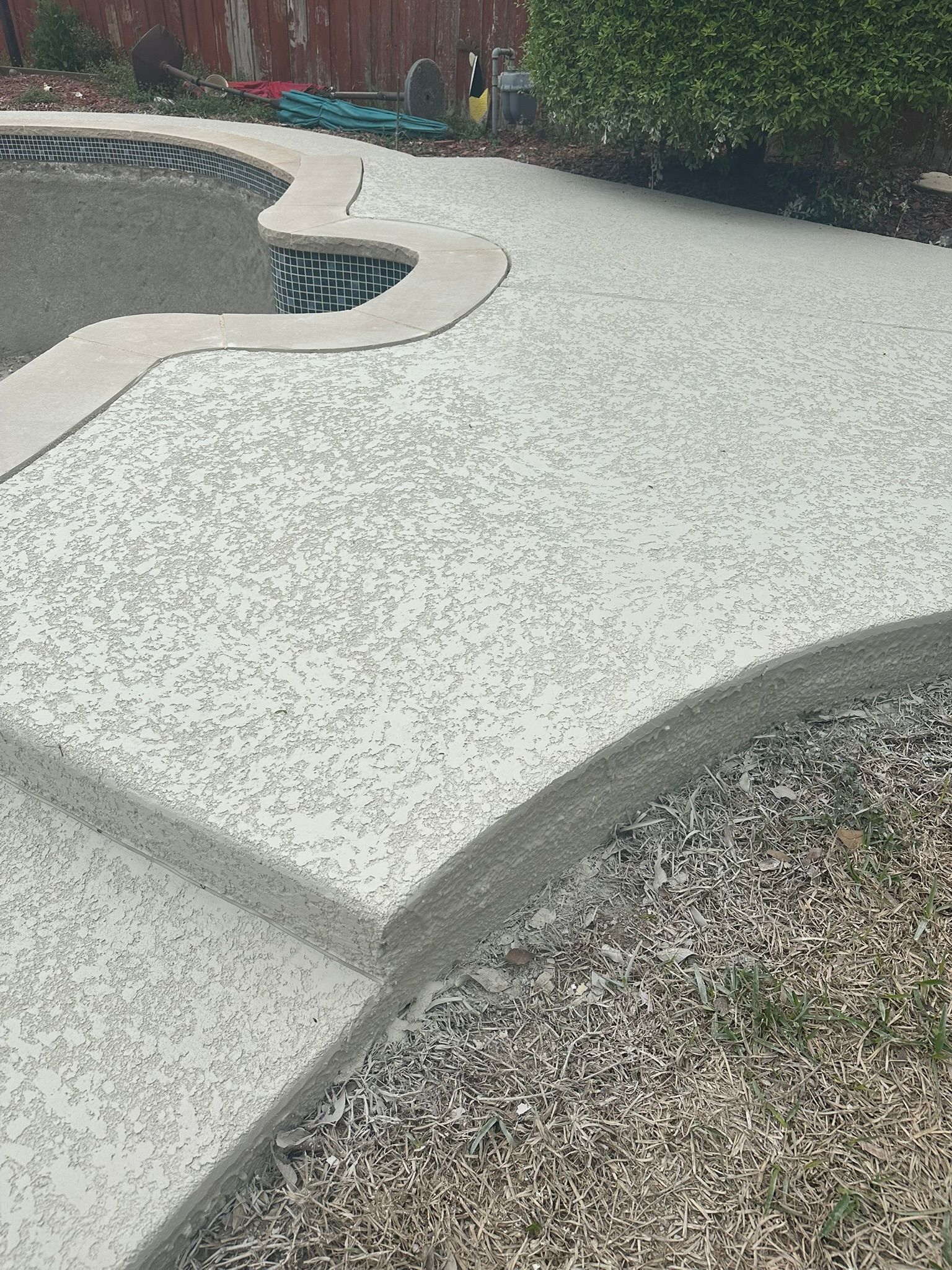 Concrete pool deck with textured finish, curved edges, and gravel border.