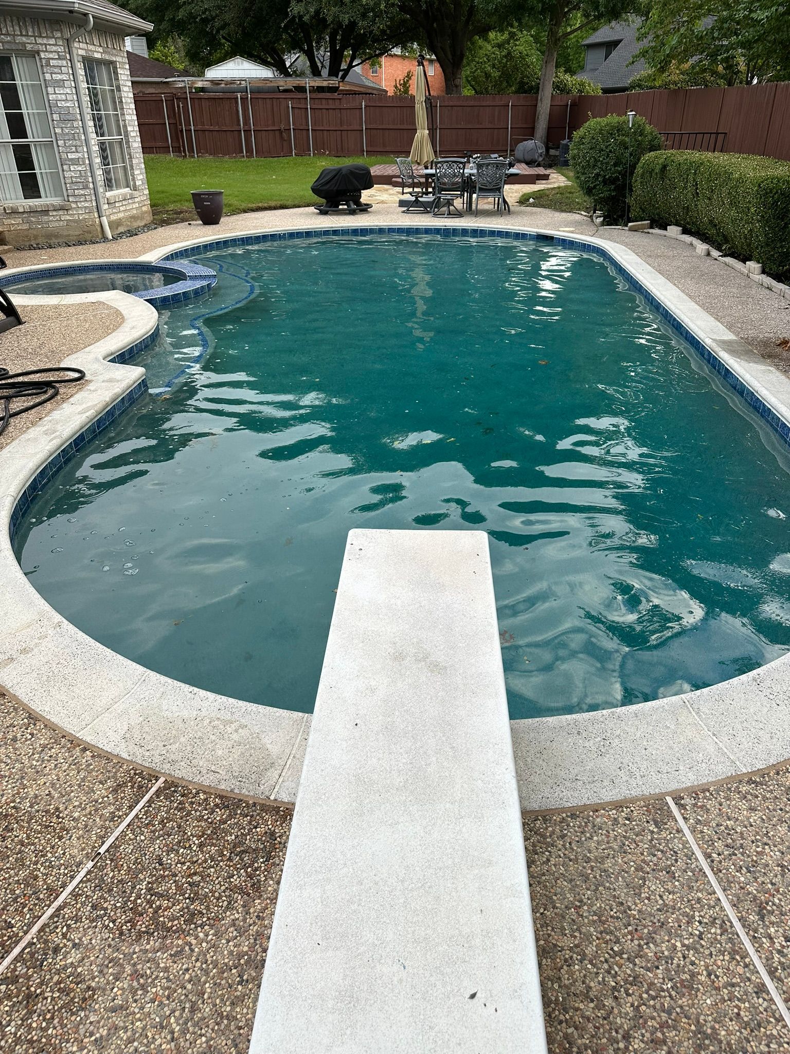 A swimming pool with a diving board in a backyard.