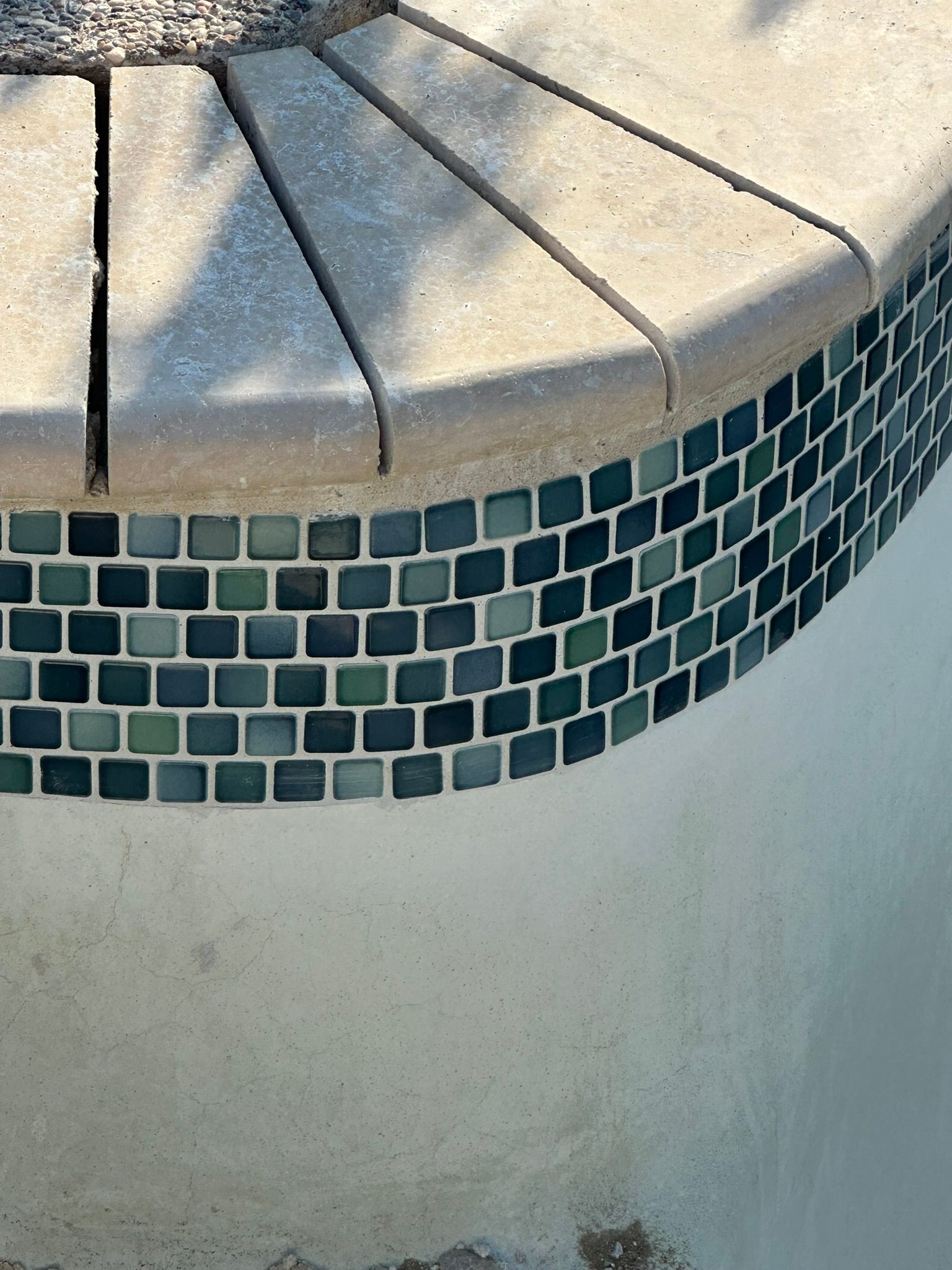 Curved pool edge with blue-green tile border and tan coping.
