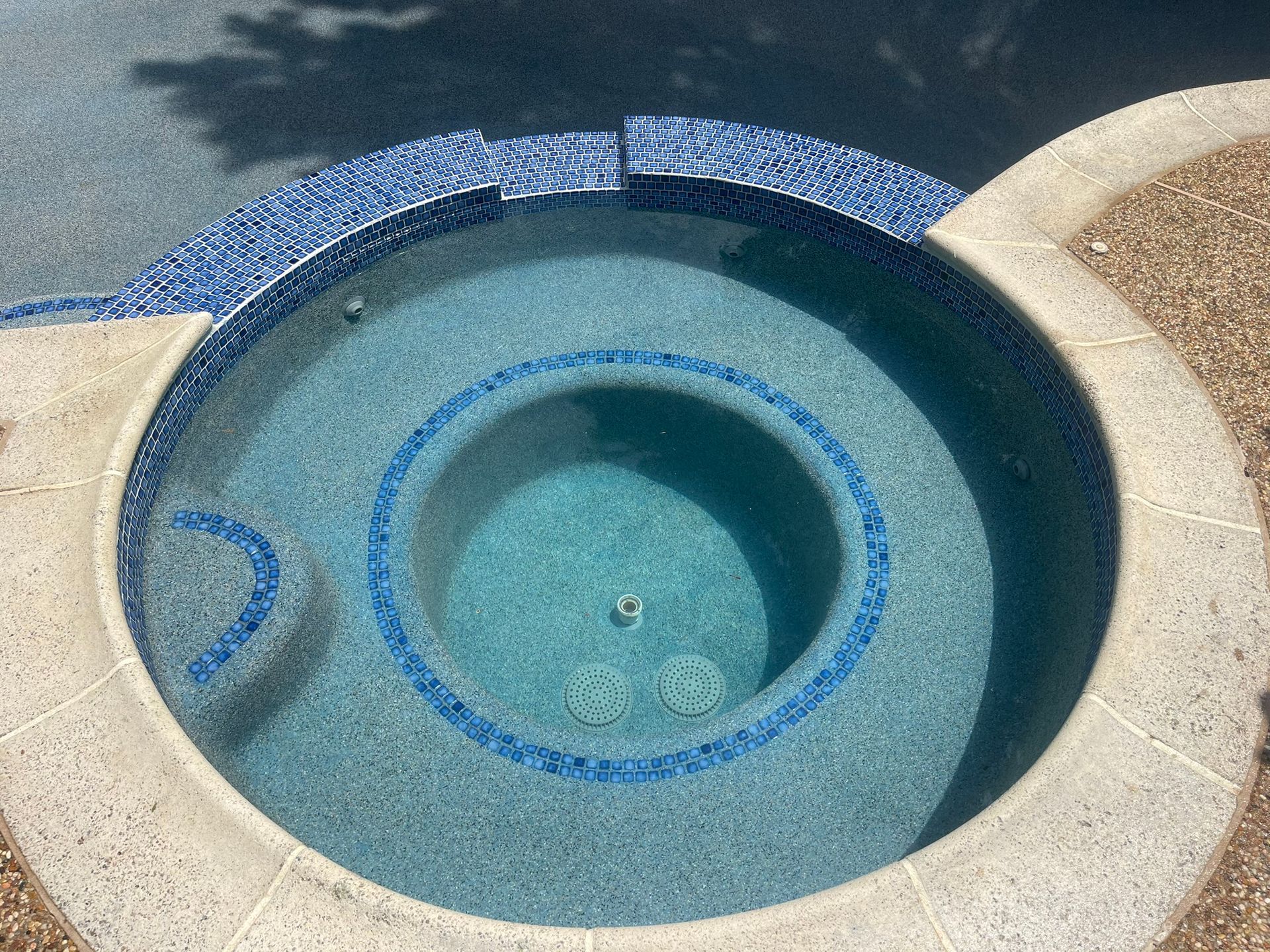 Circular pool with blue tile trim, water, and tan concrete surround.