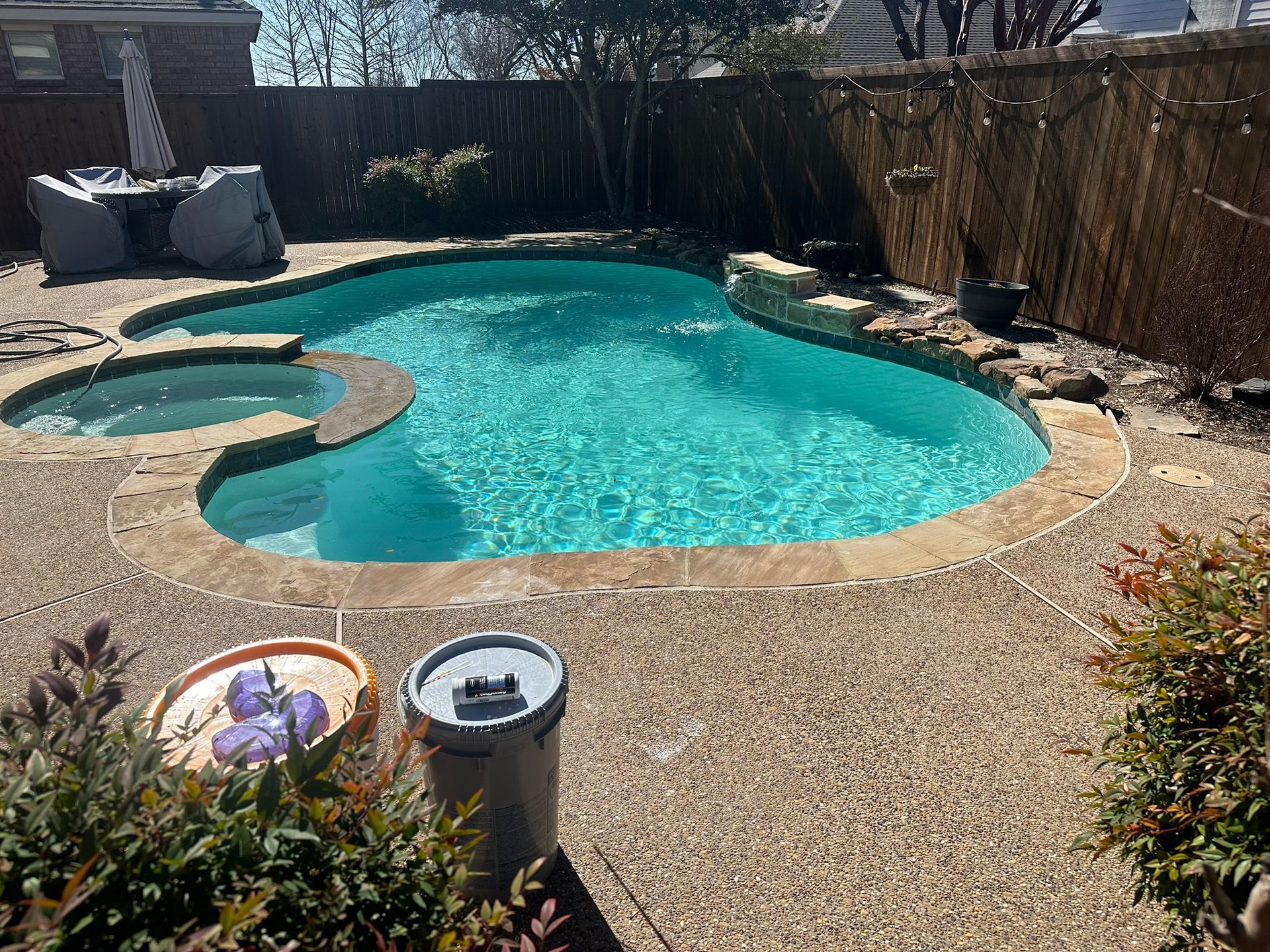 Swimming pool with spa, surrounded by stone patio, bamboo fence, and greenery.