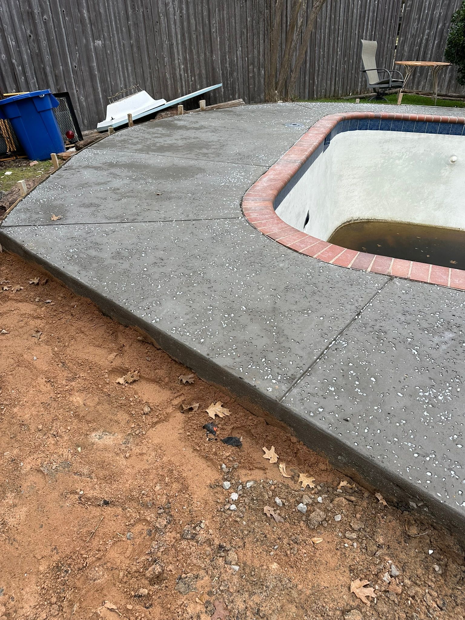 Concrete pool deck with brick border; pool is empty; adjacent dirt area.