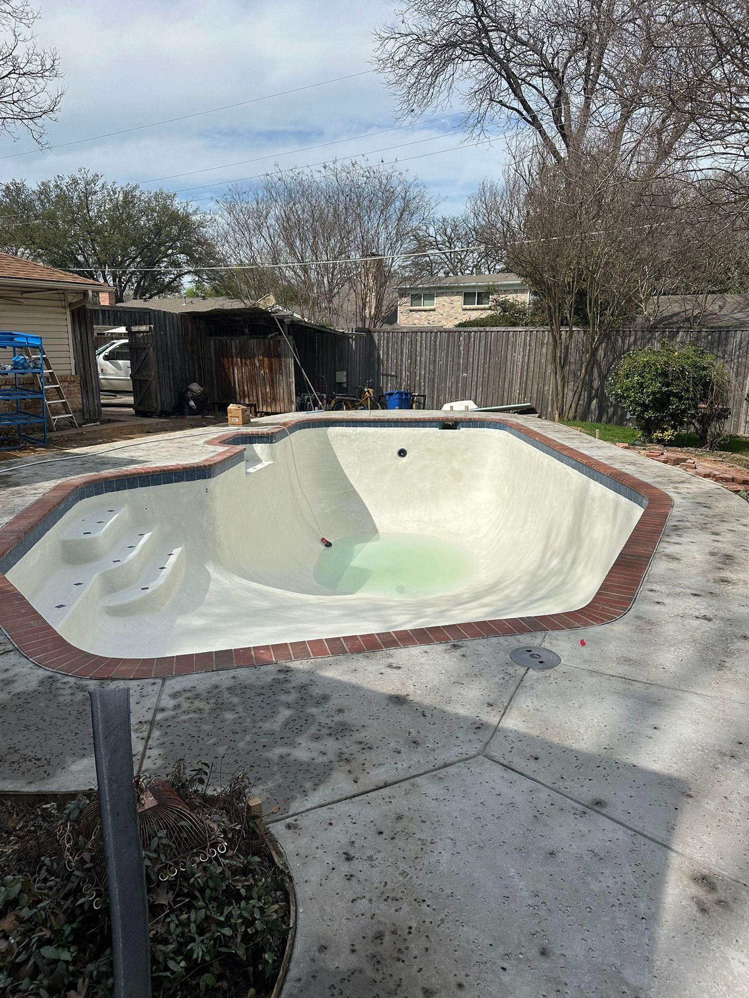 Empty swimming pool with brick trim and concrete surround in a backyard.