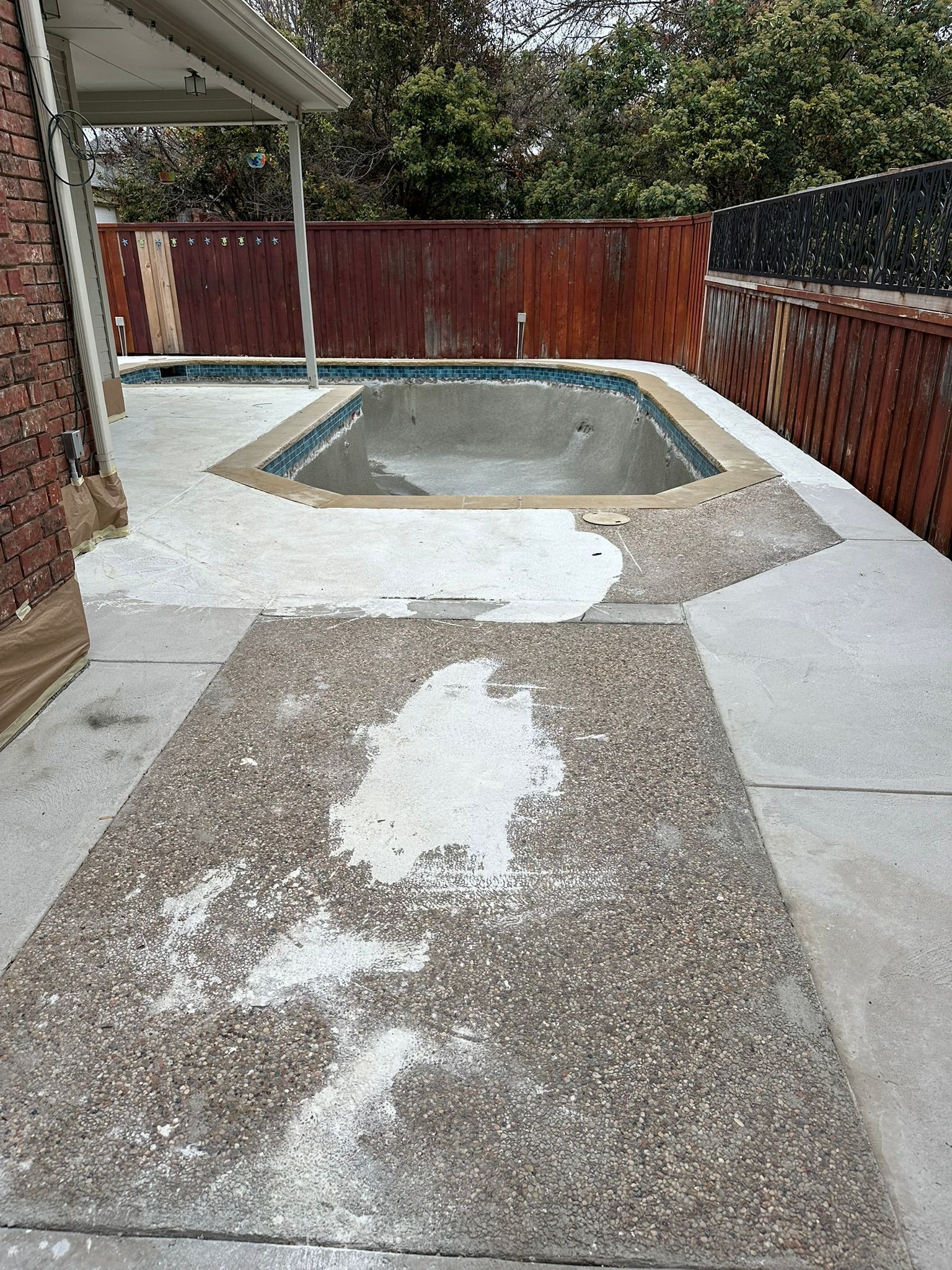 Empty pool with cracked concrete surround; wooden fence in background.