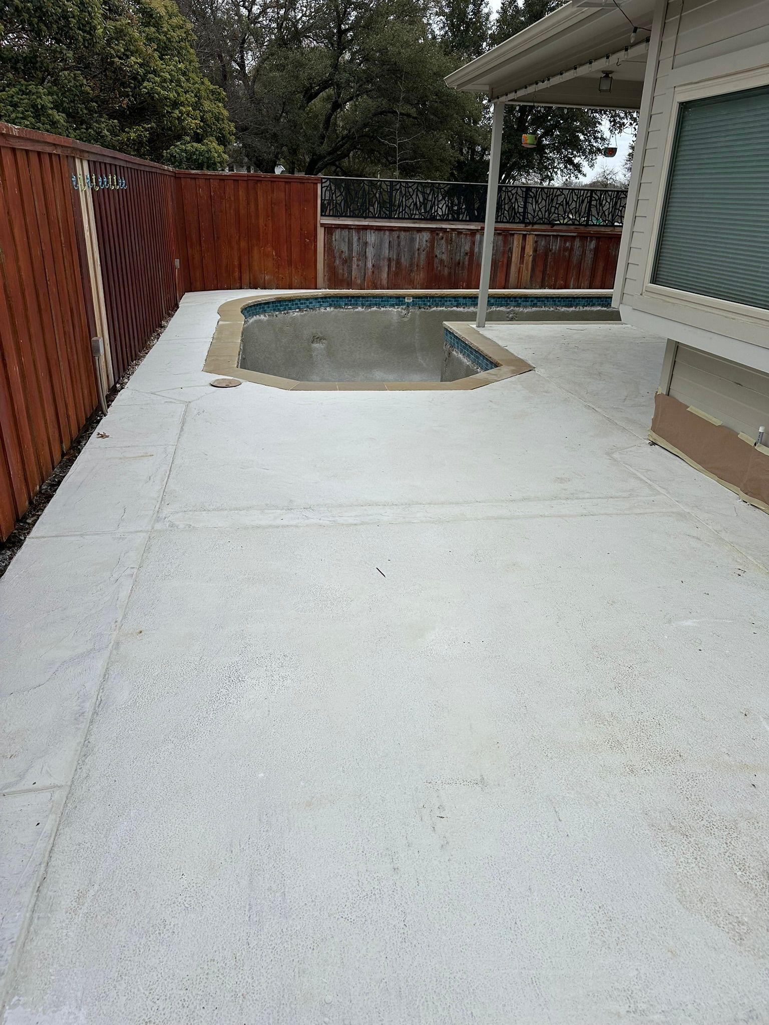Concrete patio with a small pool and a wooden fence.