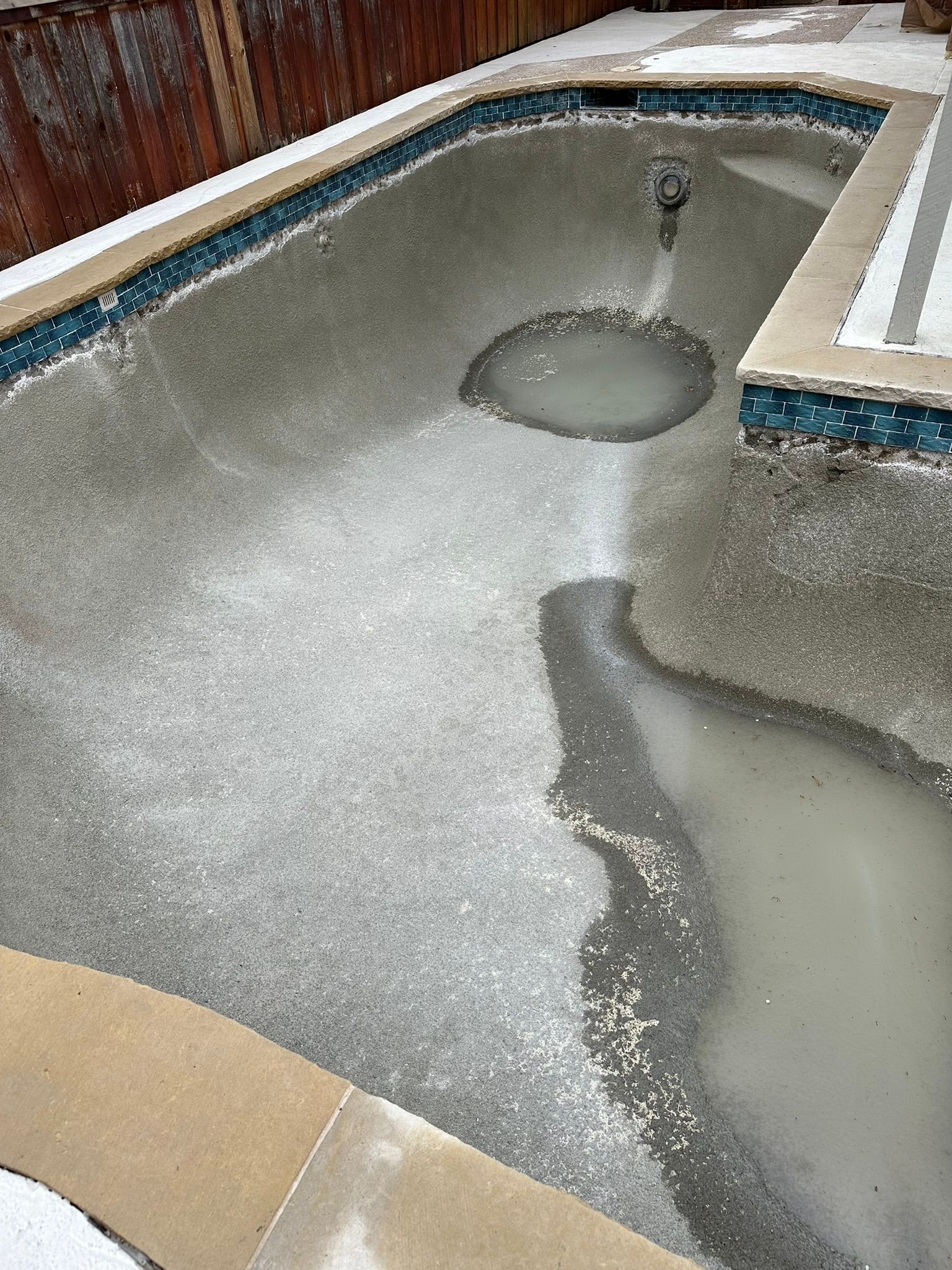 Frozen swimming pool, with patches of ice and standing water, surrounded by concrete and tiles.