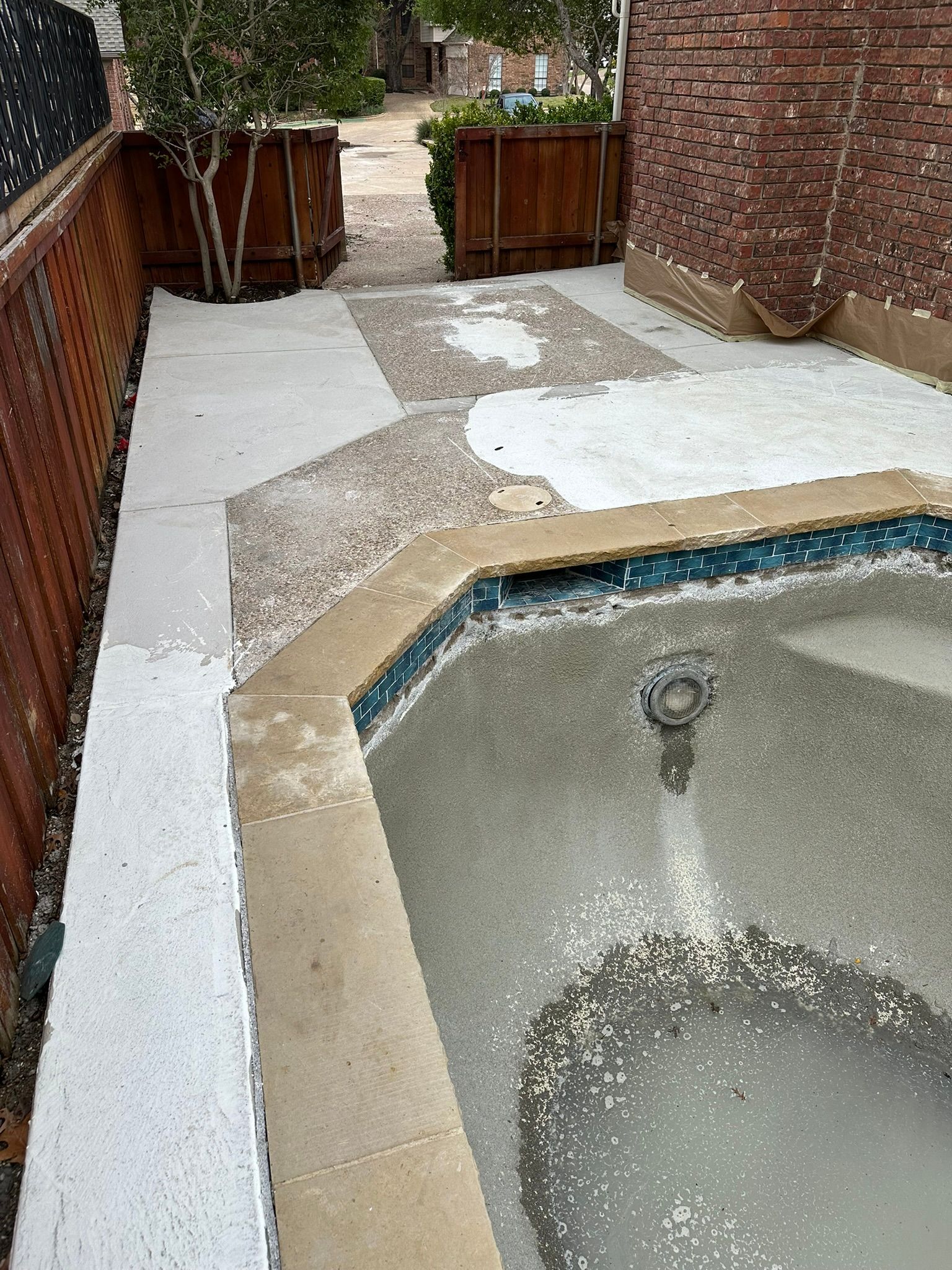 Backyard with a pool, concrete pathway, and wooden planters, bordered by a brick wall and wooden fence.