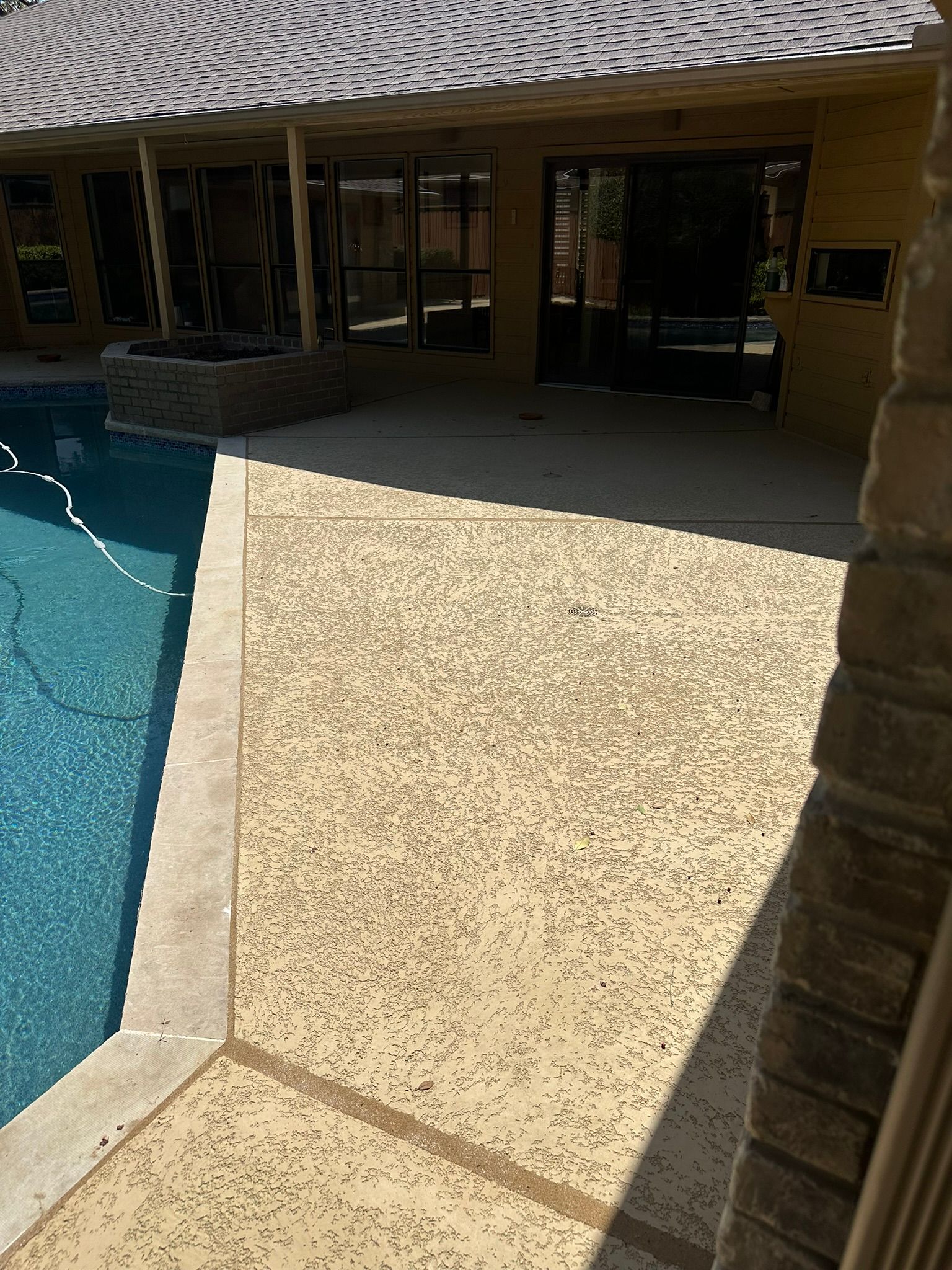 Poolside patio with textured concrete, next to a blue swimming pool, under a covered area.