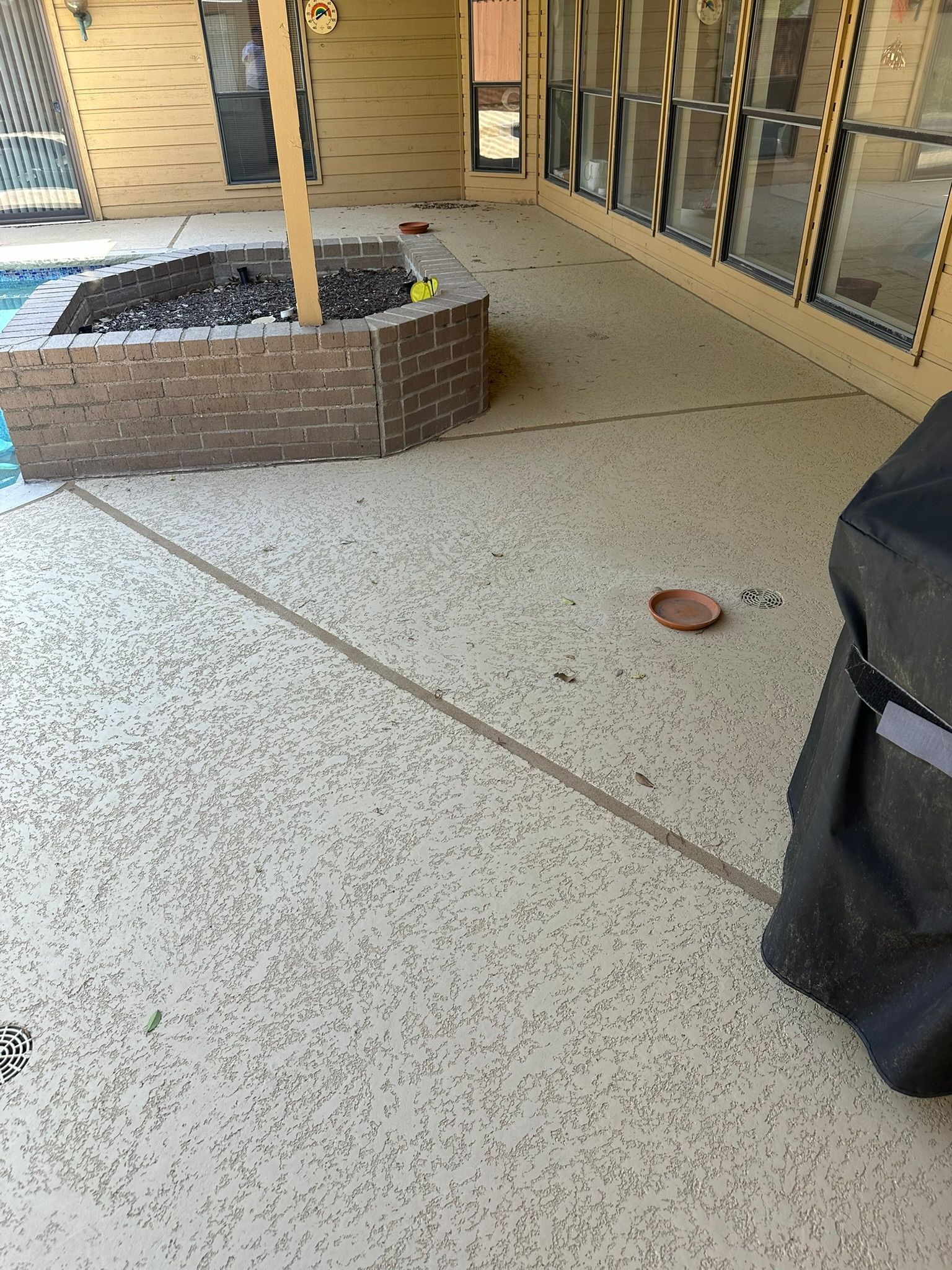 Patio with speckled concrete floor, brick fire pit, and grill covered with black case.