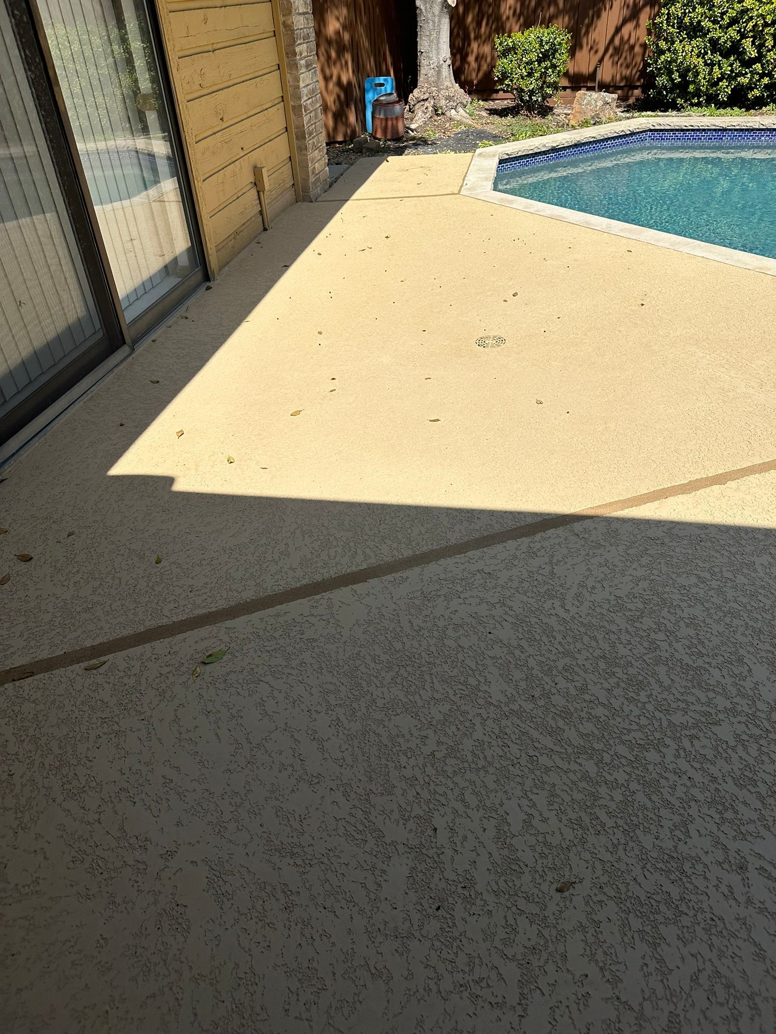 Concrete patio next to a pool with sliding glass doors.