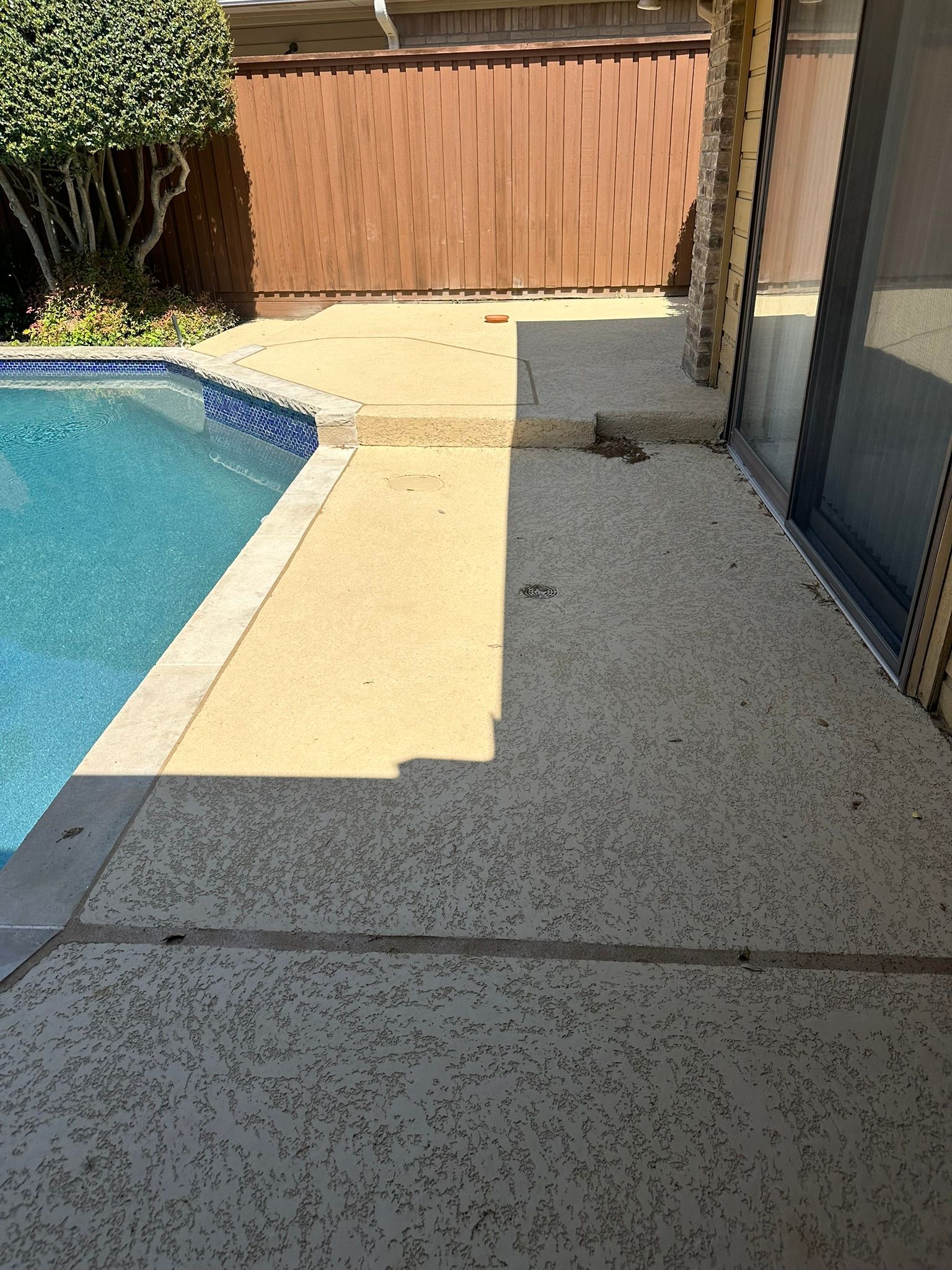 Poolside concrete patio with a fence in the background, next to a pool.