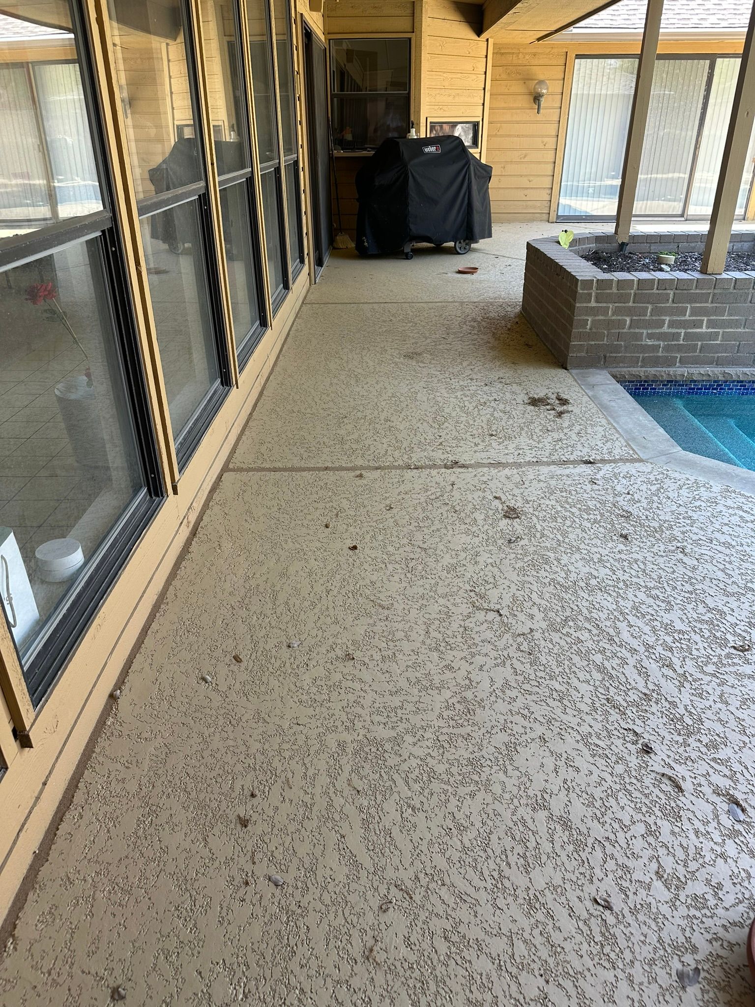 Patio with a speckled concrete floor, pool, and windows.