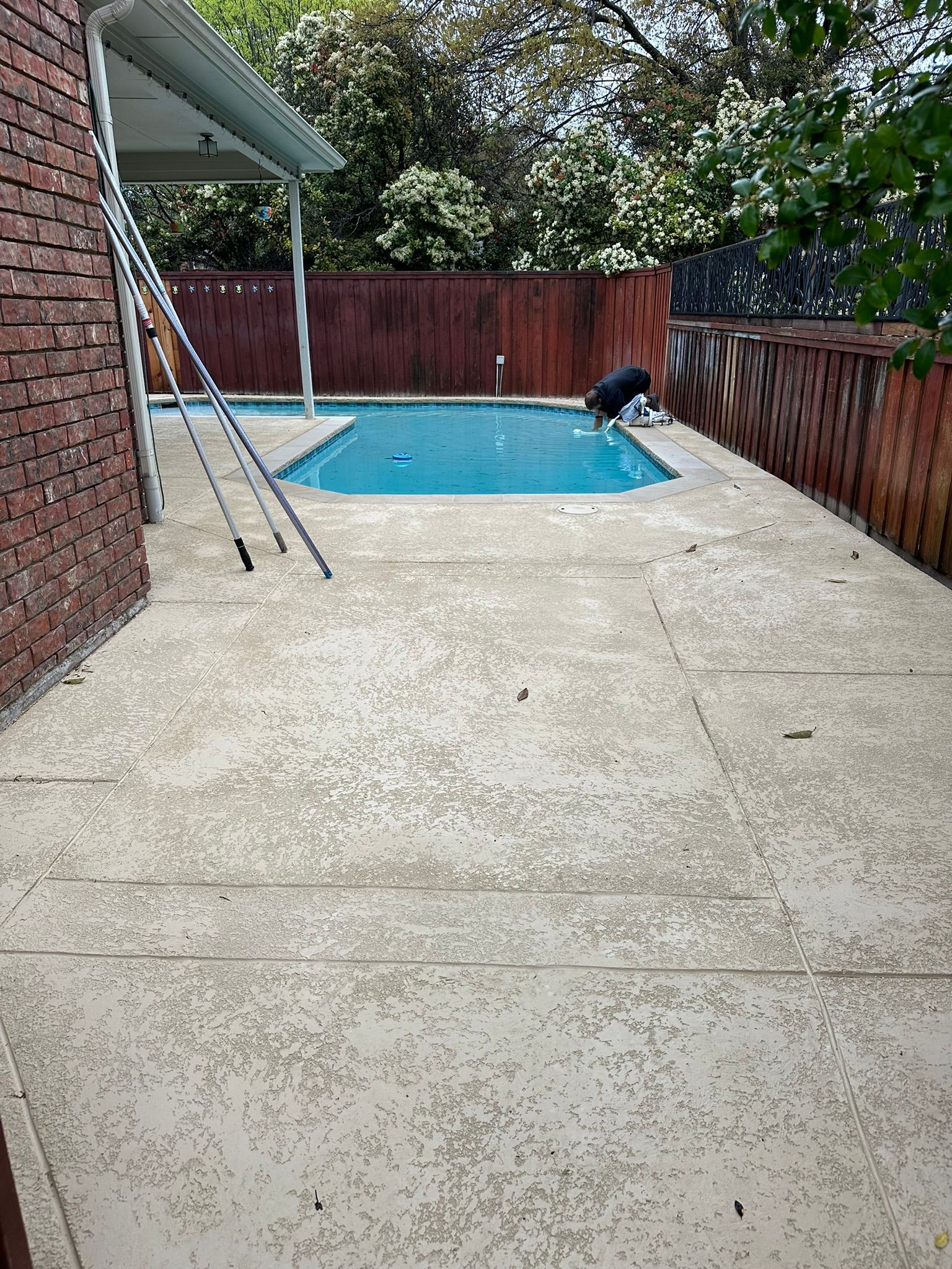 Concrete patio with a small pool, wooden fence, and brick wall. A person is near the pool.