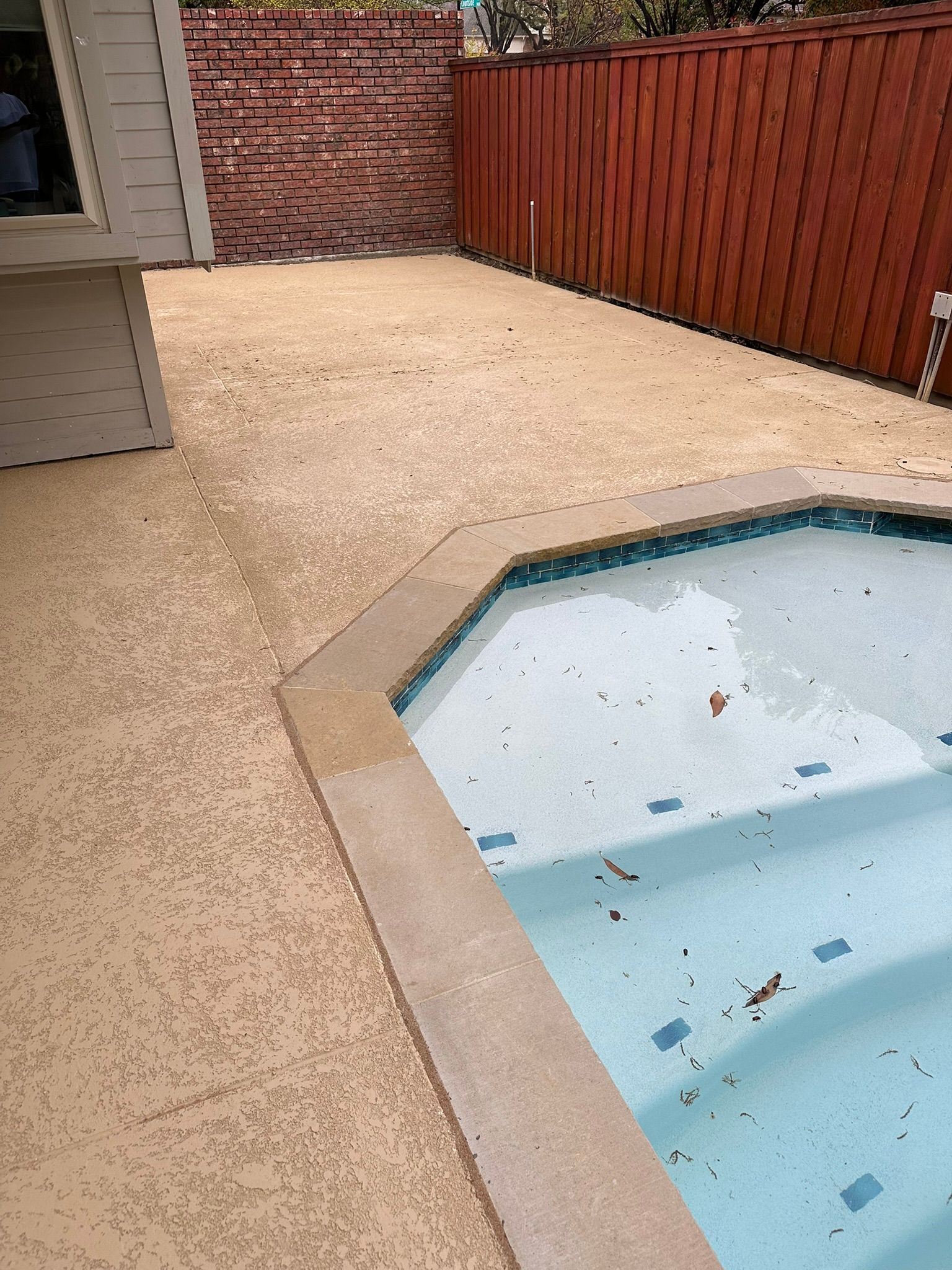 Concrete patio with pool, surrounded by brown fence and brick wall.