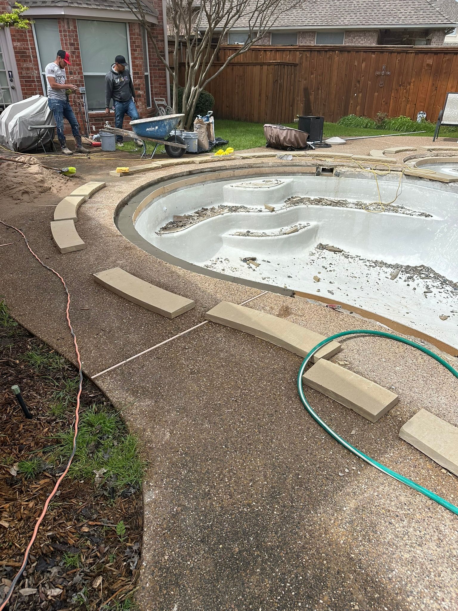 Construction workers installing paving stones around a pool.