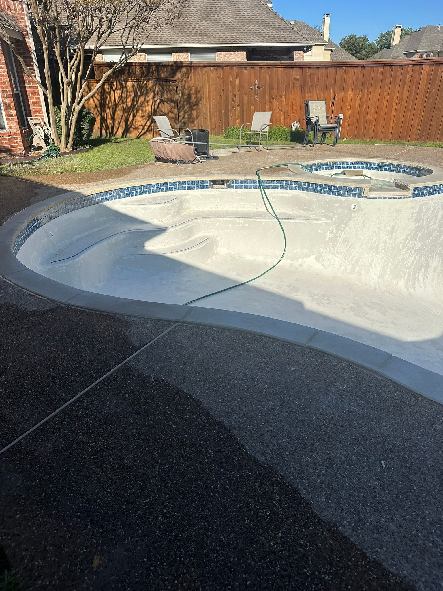 Backyard with an empty swimming pool and concrete patio. Wooden fence and house in the background.