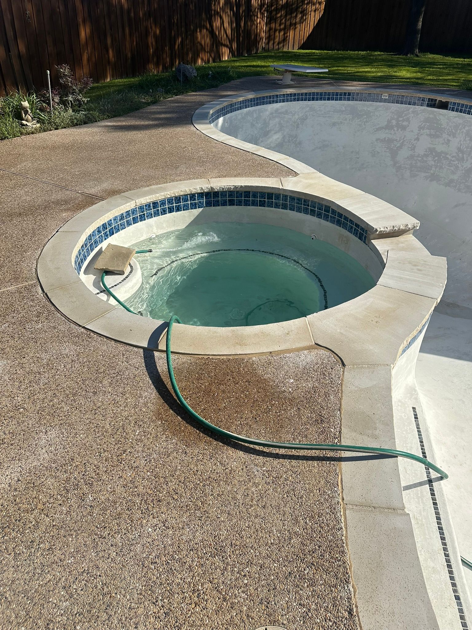 A partially filled hot tub with a swirling water inside; next to a partially filled swimming pool.