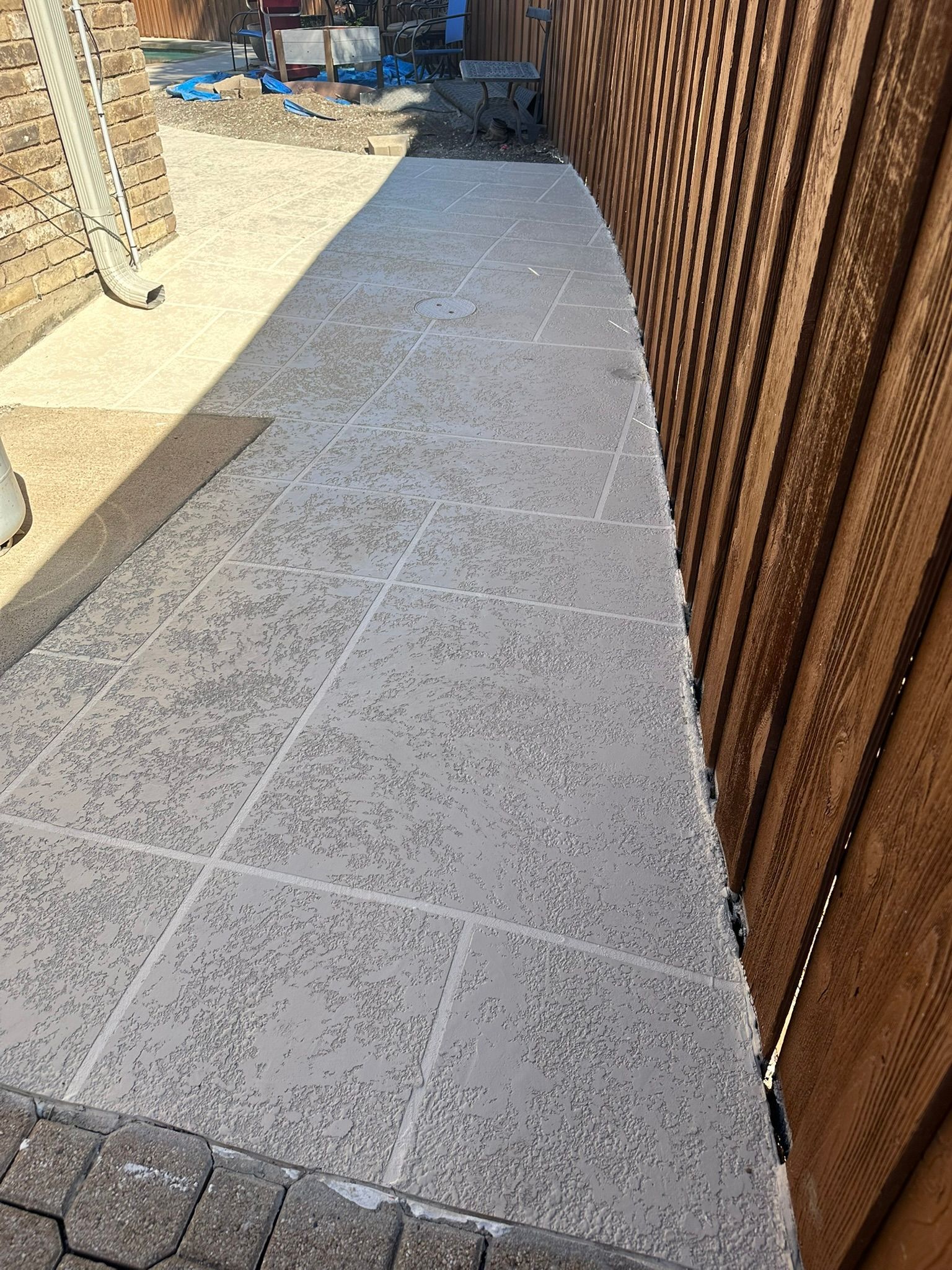 Pathway of light-colored stone tiles next to a wooden fence. Construction equipment visible in the background.