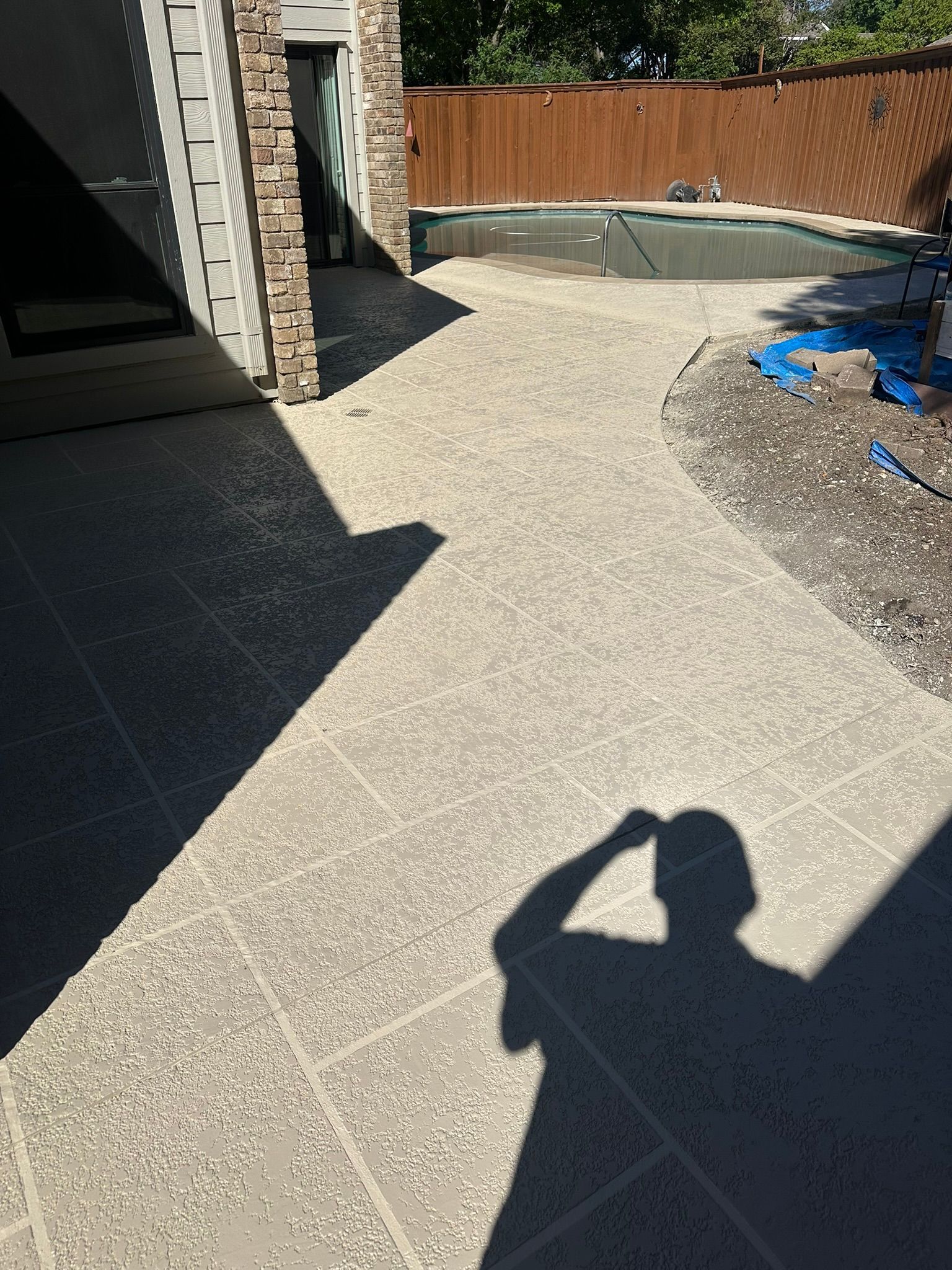 Concrete patio with a pool in the background and a shadow of a person.