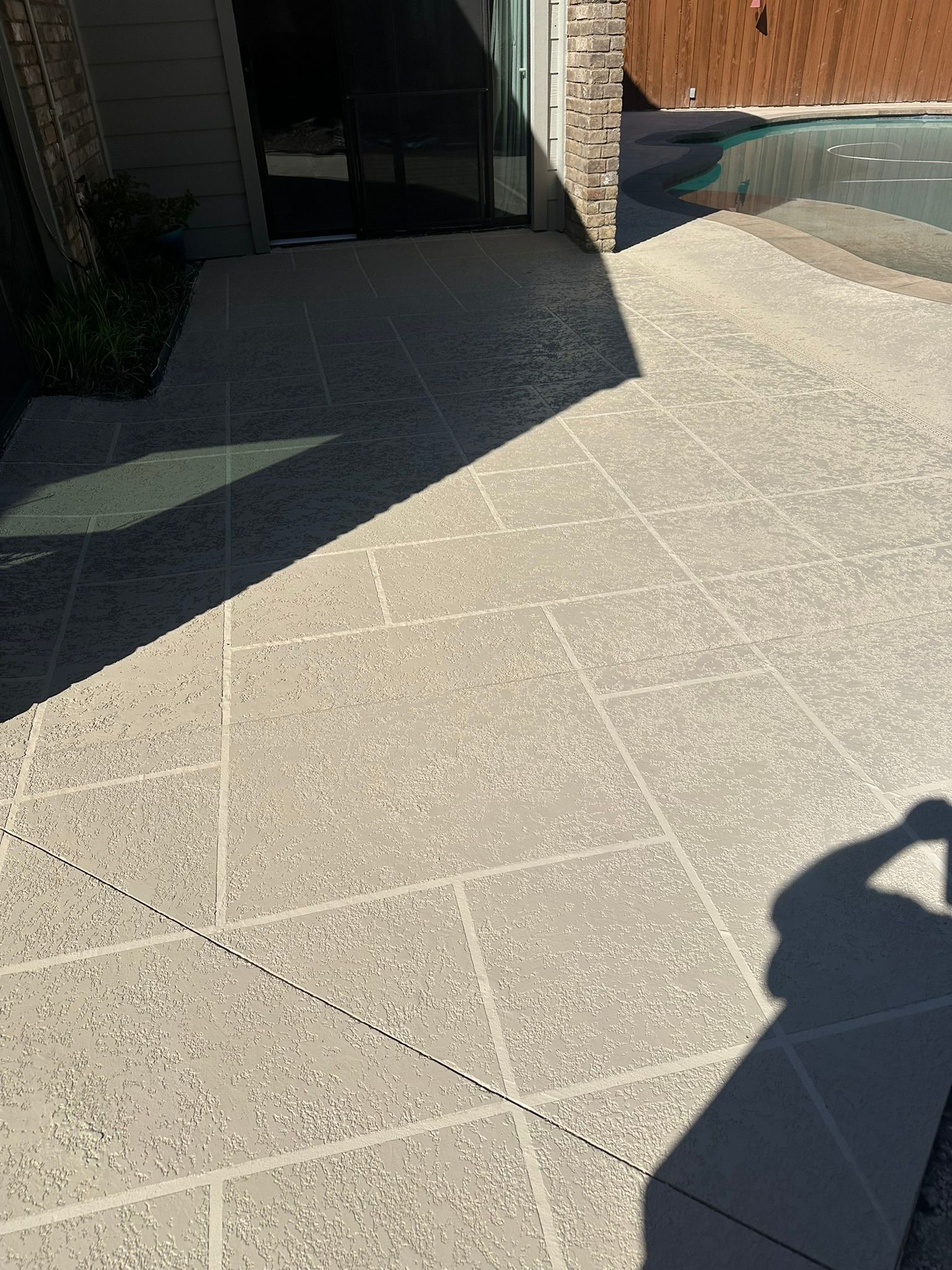 Concrete patio with a patterned surface, next to a pool and a house entrance.
