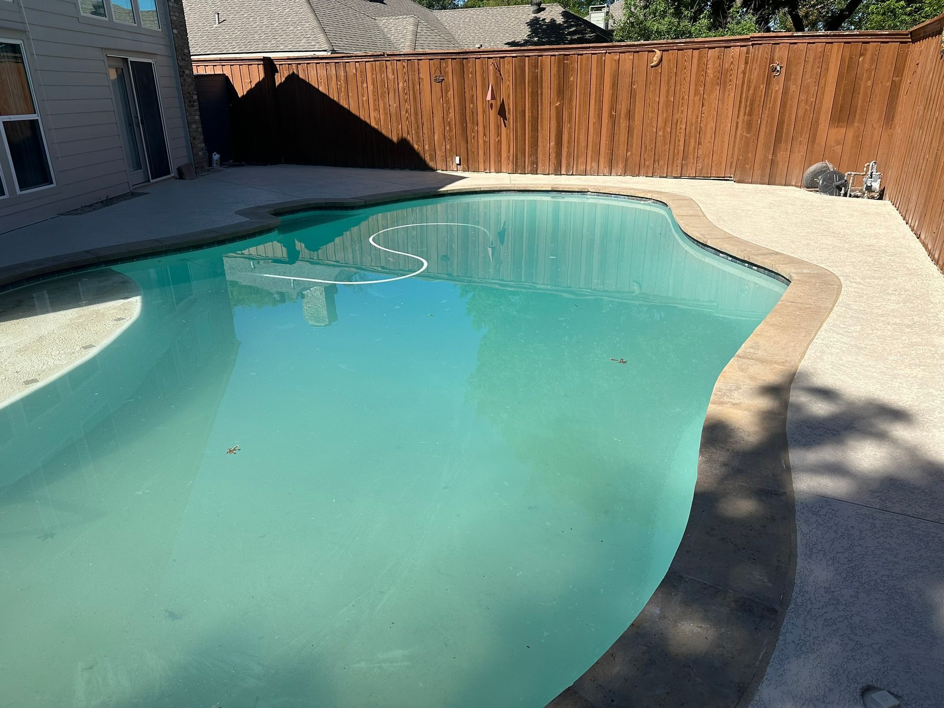 Swimming pool with turquoise water, surrounded by concrete and a brown wooden fence.