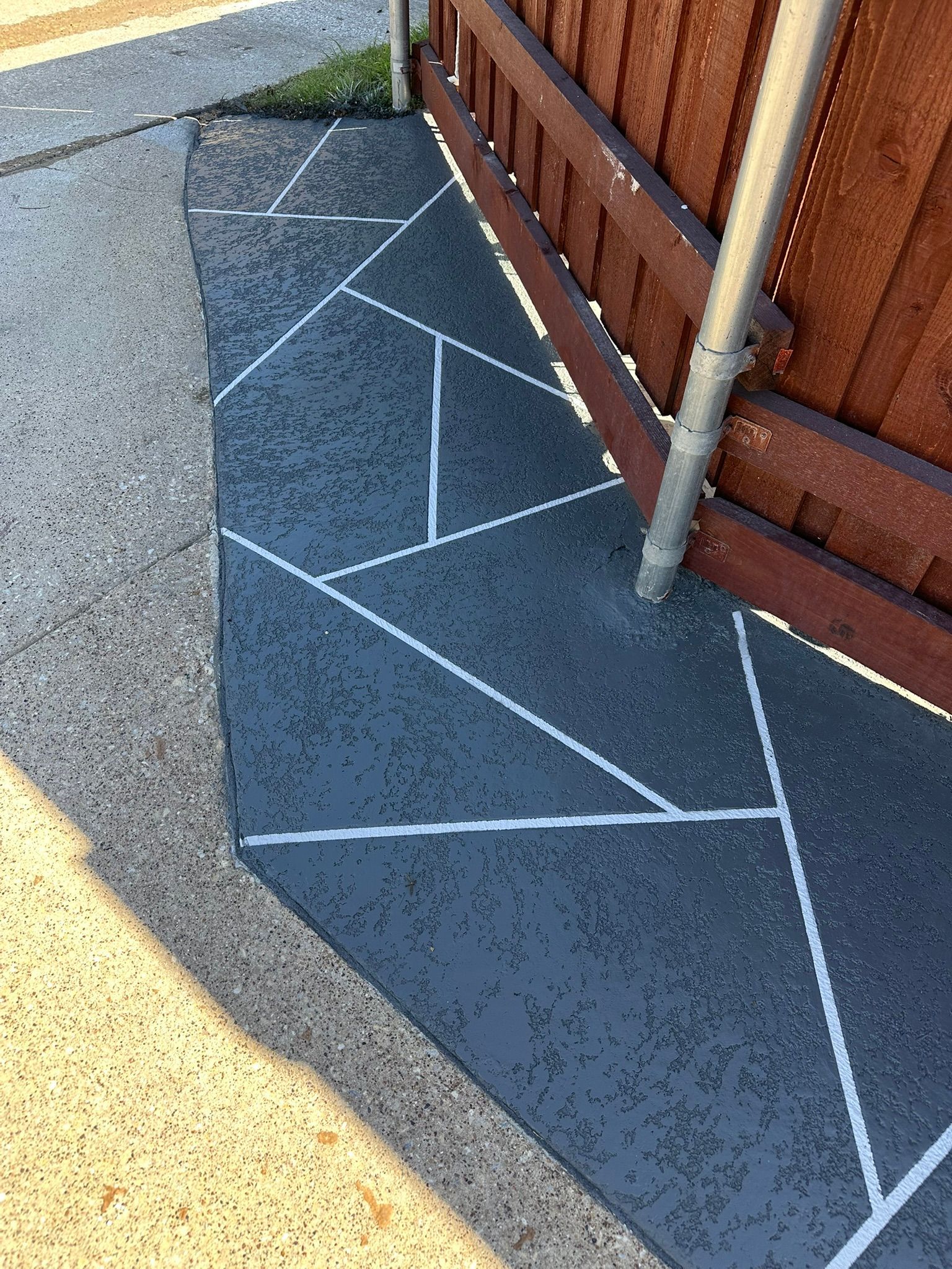 Concrete sidewalk with gray and white geometric pattern next to a wooden fence.