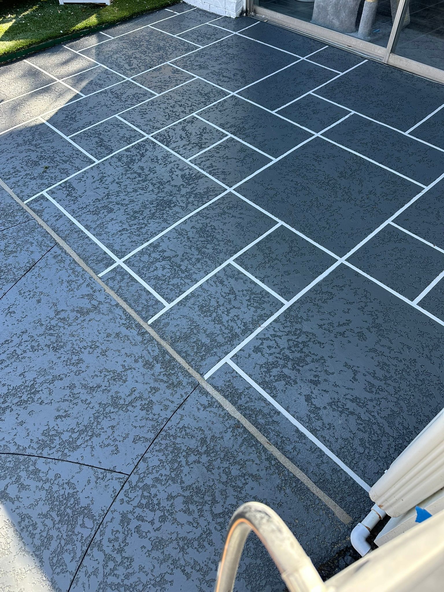 Gray patio with white grid lines, next to a pool with a metal railing.
