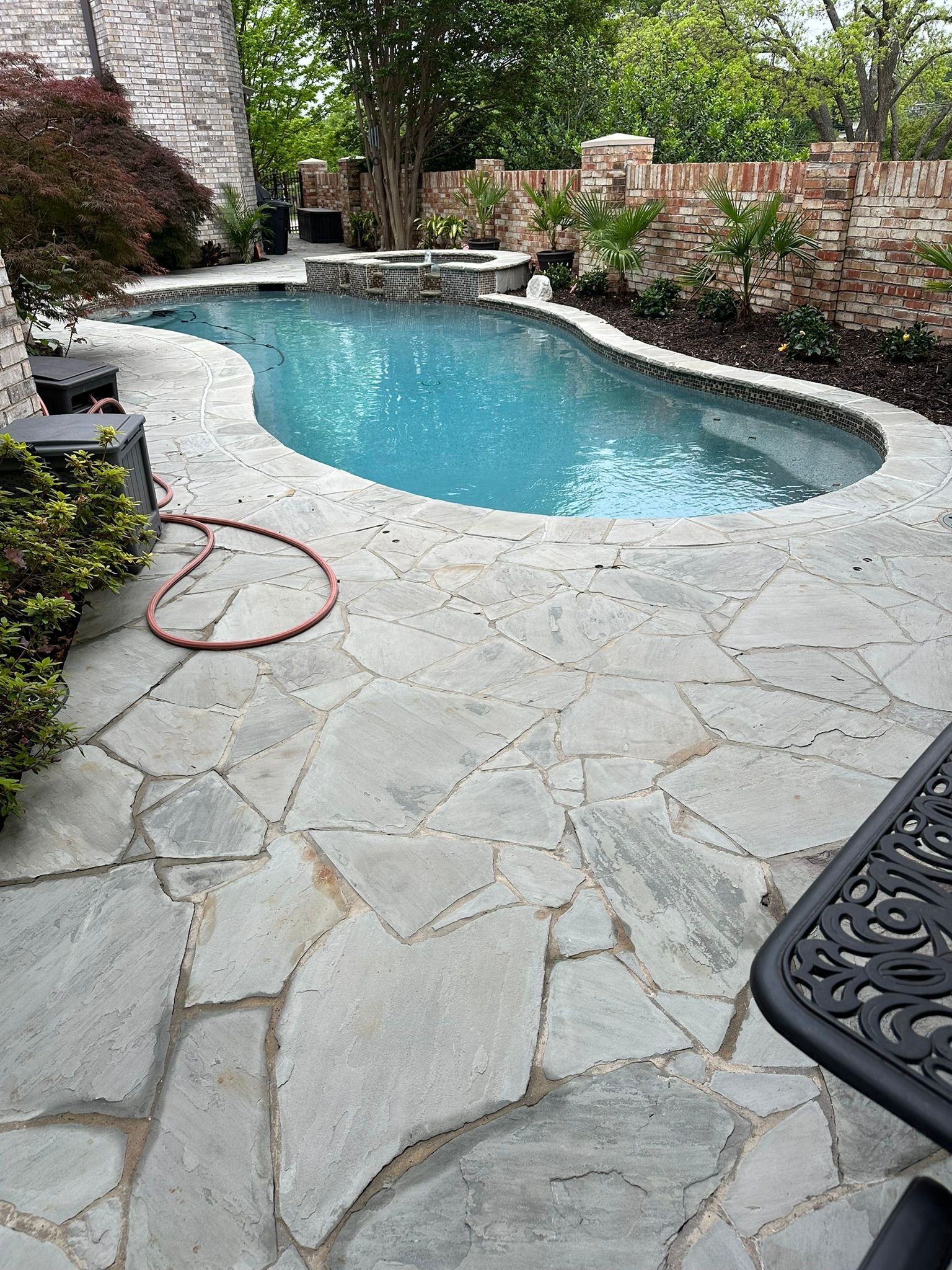 Pool and patio area with blue water, gray stone pavers, and a brick wall.