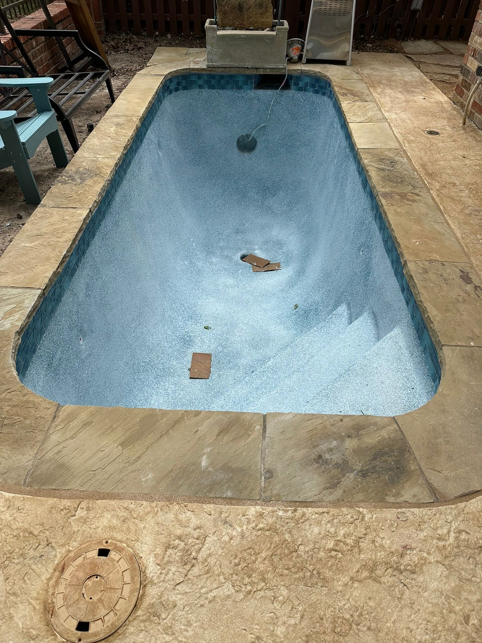 Small rectangular swimming pool with blue speckled lining, surrounded by stone paving.