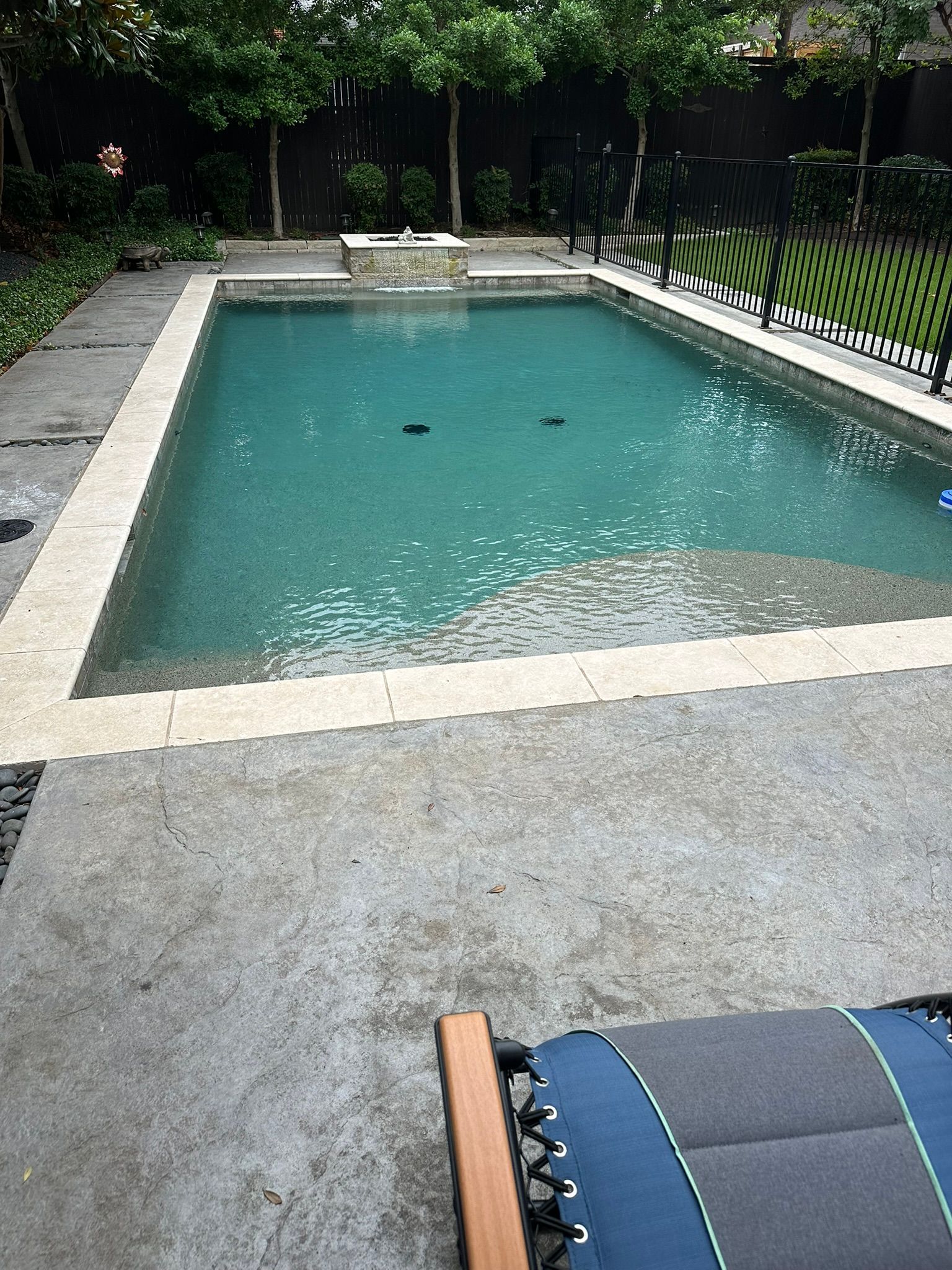 Rectangular swimming pool surrounded by stone and concrete patio; outdoor setting.