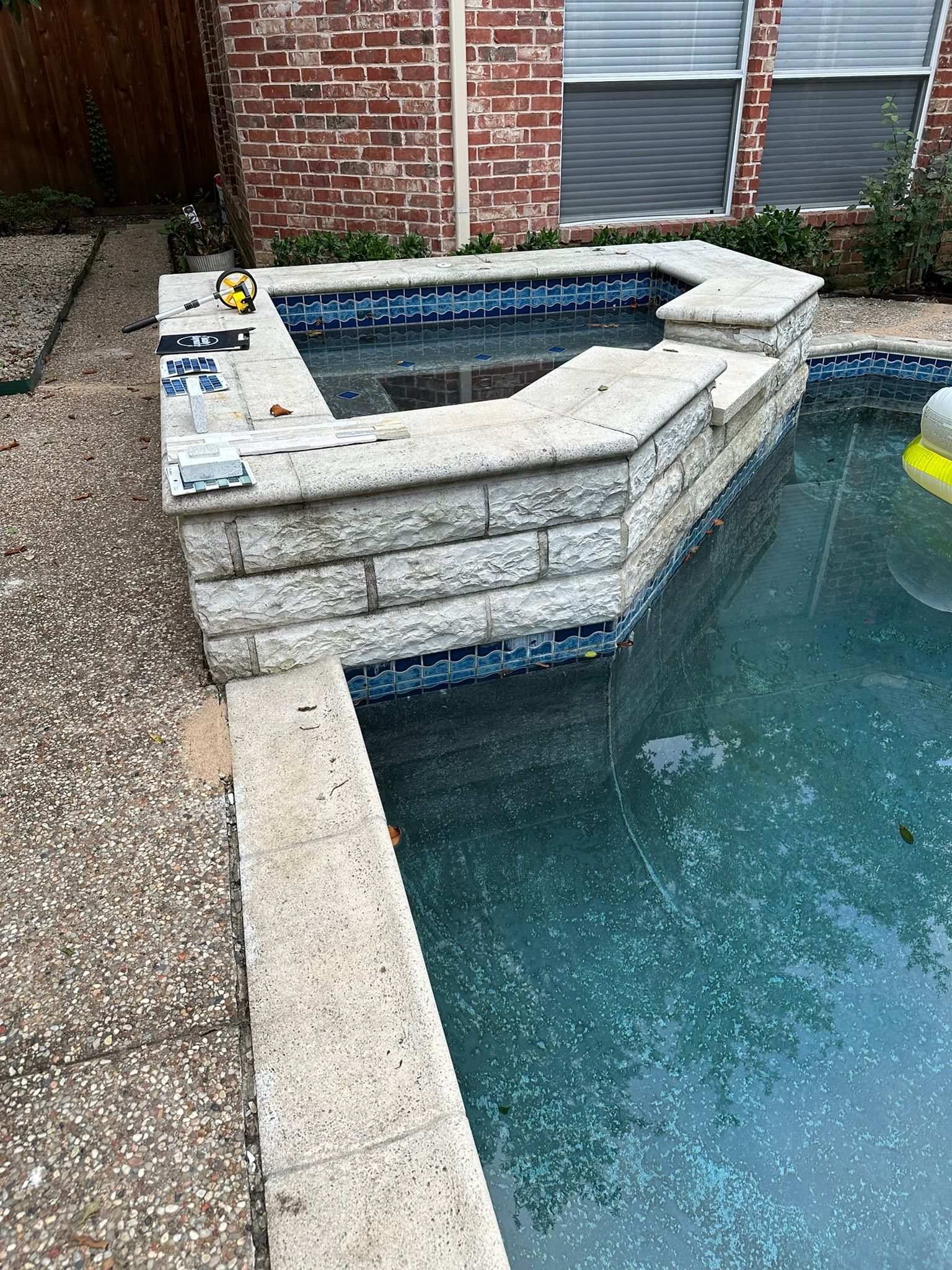 Swimming pool with raised spa area, stone brick design, water is blue, exterior setting.