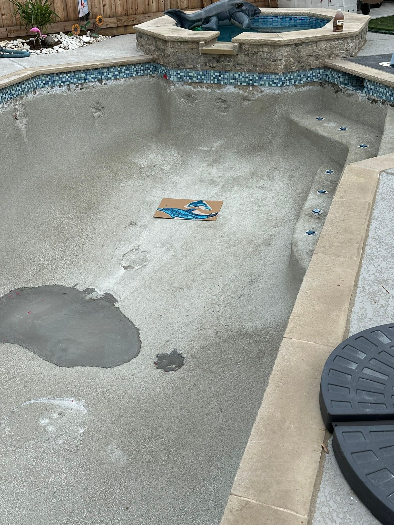 Empty swimming pool with pebble finish and attached hot tub.